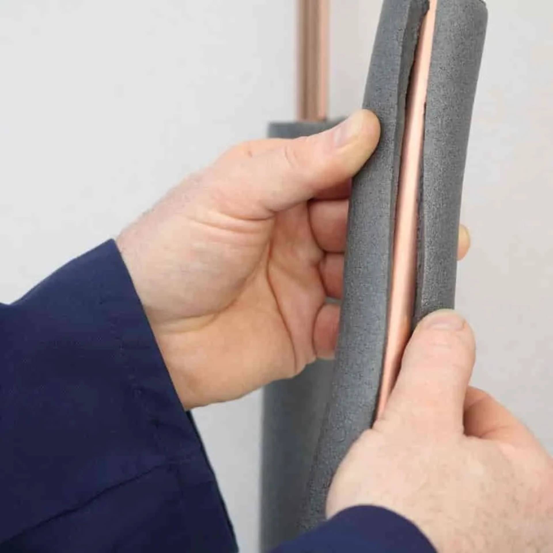 Hände drücken graue Schaumisolierung um ein Kupferrohr, zeigt Installation oder Reparatur von Rohrisolierung.