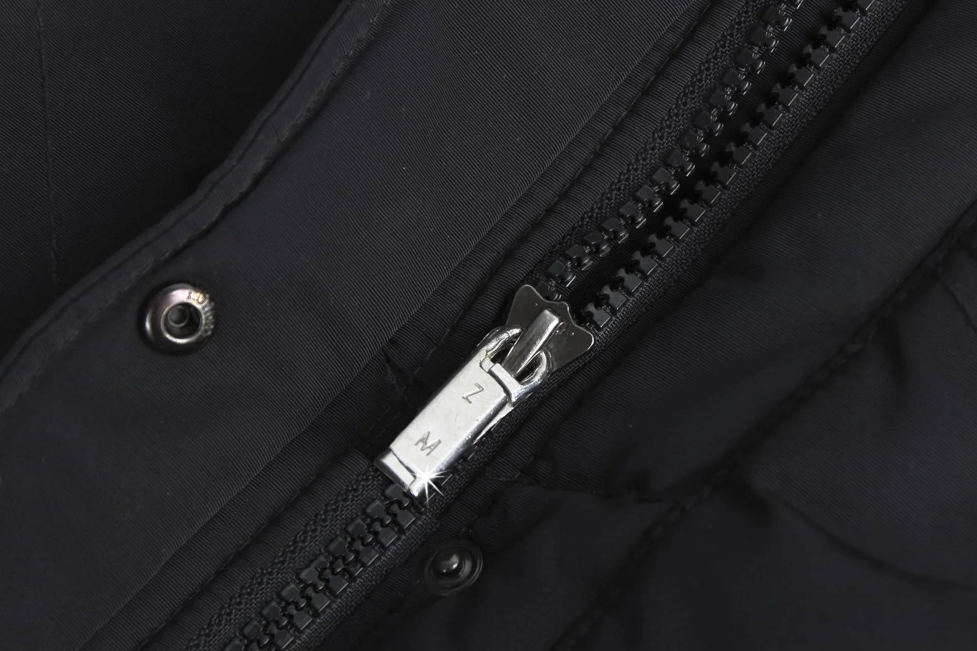Nahaufnahme eines schwarzen Jackenzippers mit silbernem Schieber, das Details der Kleidungsbefestigung zeigt.