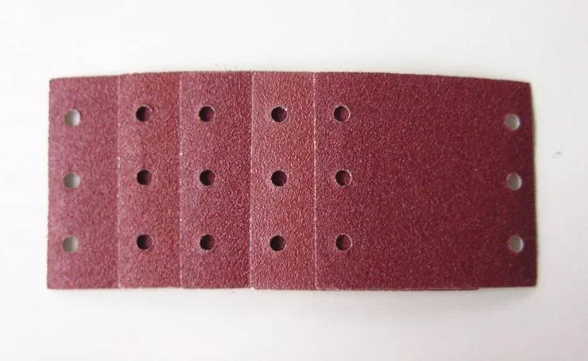 Ein Streifen rotes Schleifpapier mit mehreren gestanzten Löchern, die in vertikalen Reihen auf weißem Hintergrund angeordnet sind.
