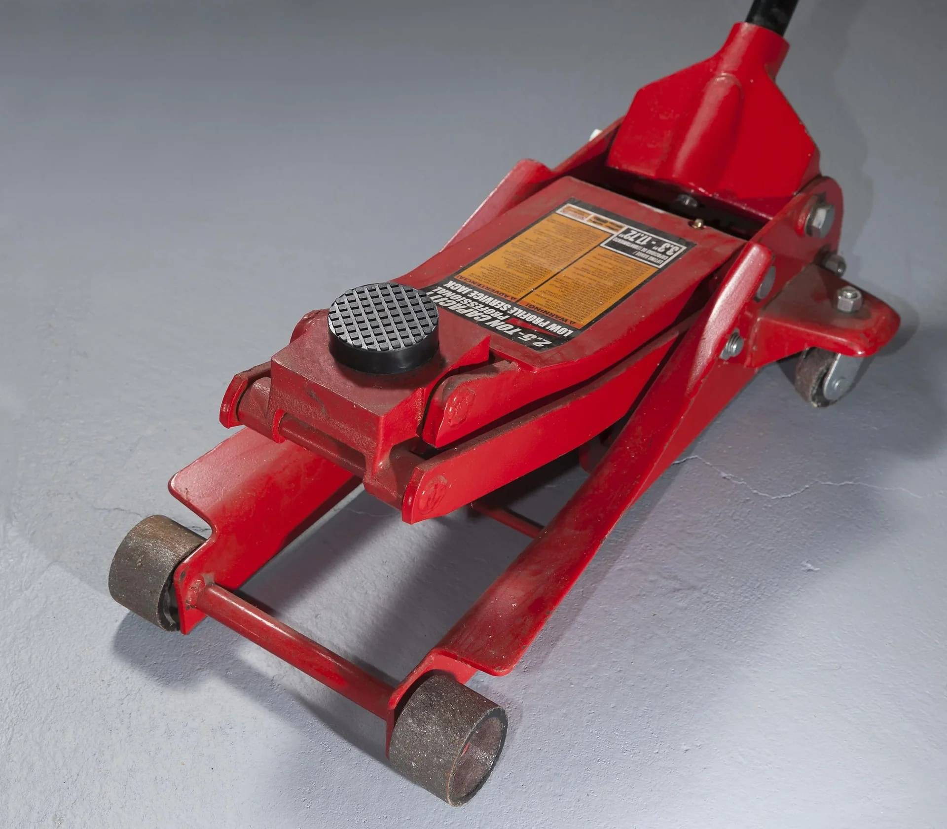 Roter hydraulischer Rangierwagenheber mit zwei vorderen Rädern und einem Hubarm, gezeigt auf einem grauen Boden.