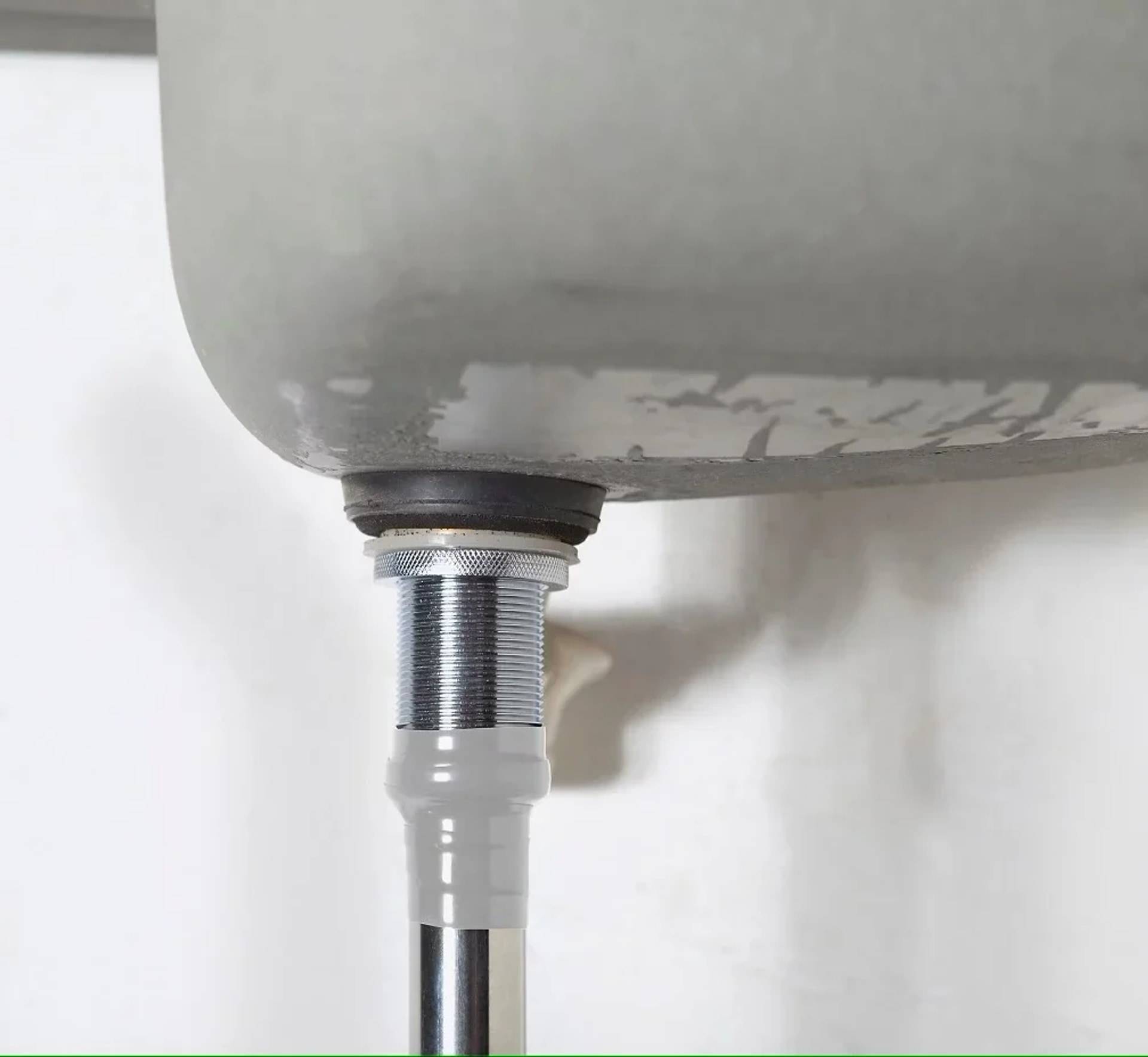 Nahaufnahme einer Waschbeckenablaufrohrverbindung mit einer Gewindemetallarmatur und einer weißen Kunststoffkupplung unter dem Becken.