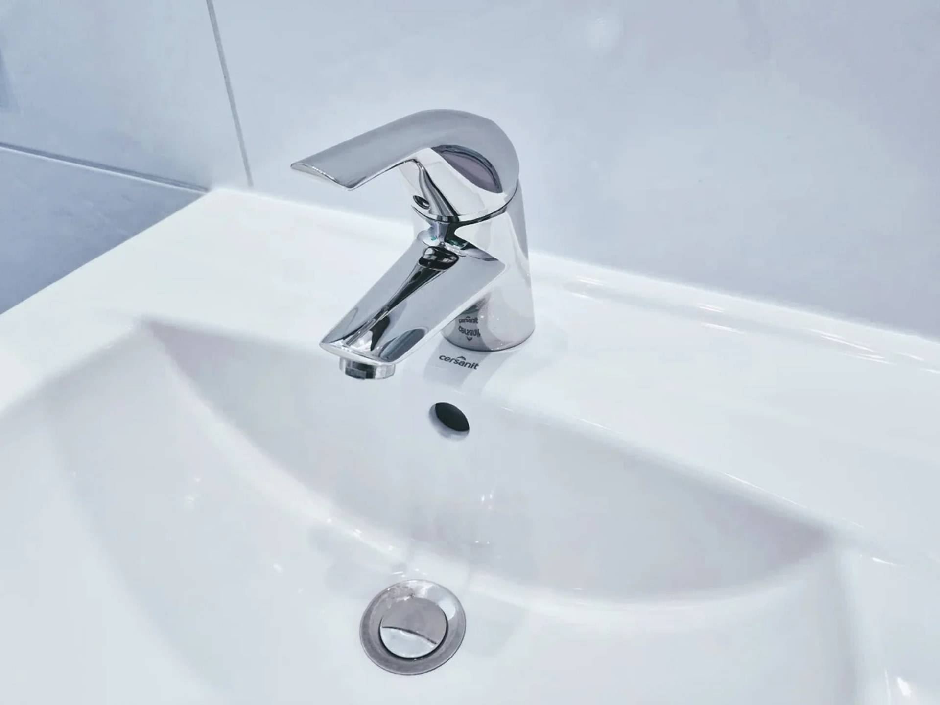 Chromglänzender Badezimmerwasserhahn über einem weißen Waschbecken, mit Wasser, das in das Becken fließt.