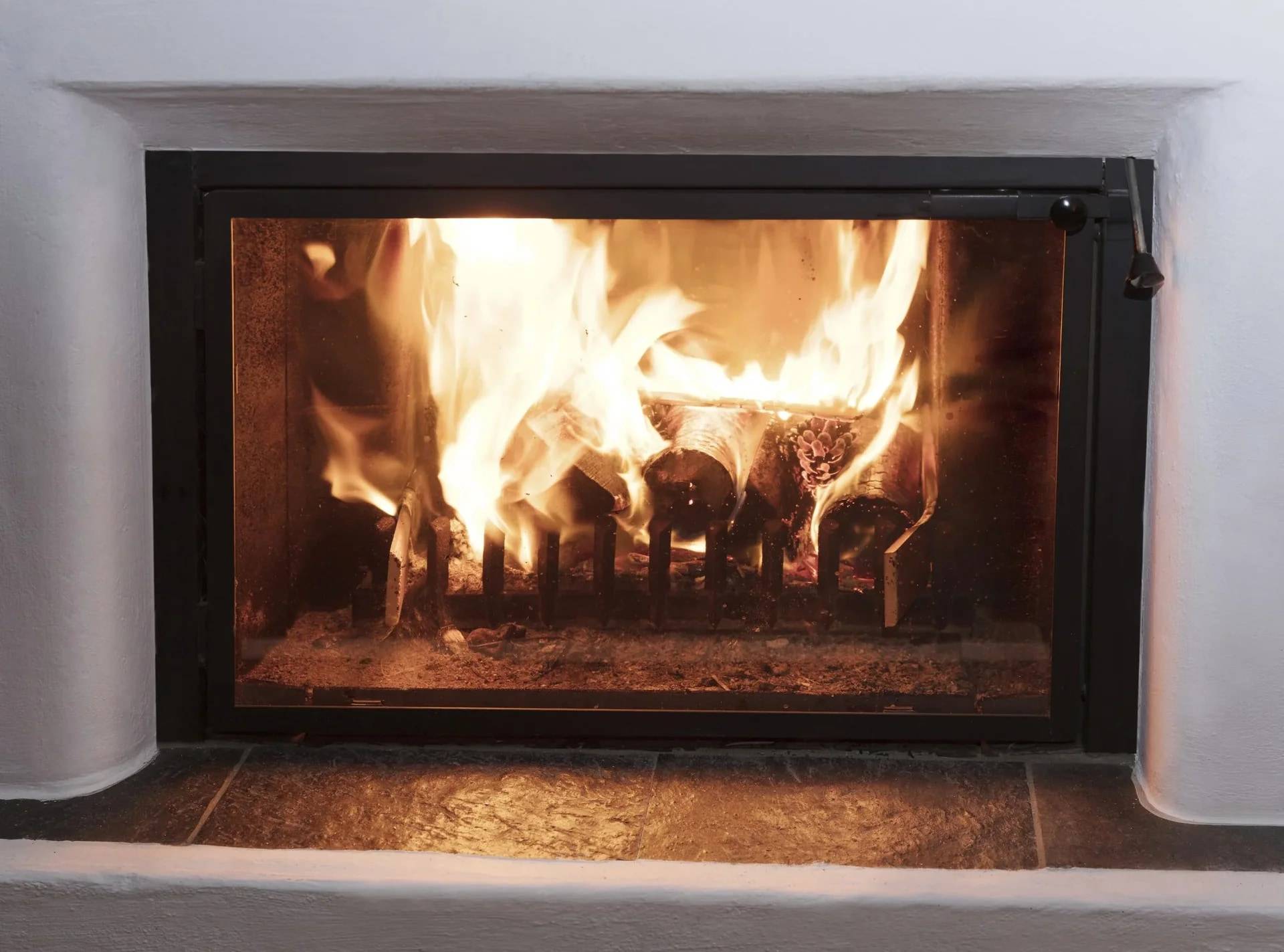Feuer, das in einem schwarzen Glaskamin brennt, der in einen weißen Kamin eingebaut ist, mit einem gefliesten Boden davor.