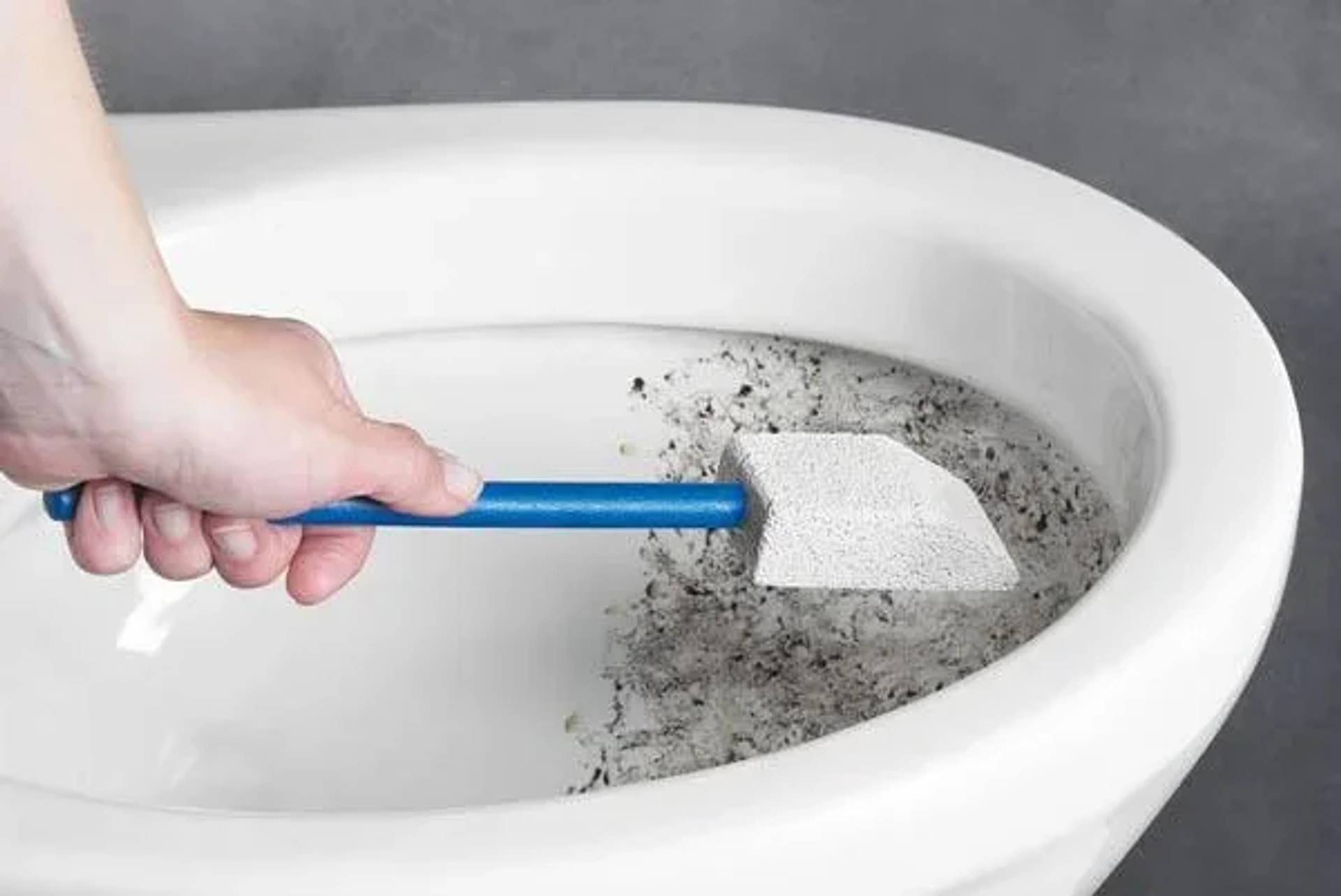 Hand reinigt eine Toilettenschüssel mit einer Bürste mit blauem Griff und schrubbt hartnäckigen dunklen Schmutz weg.
