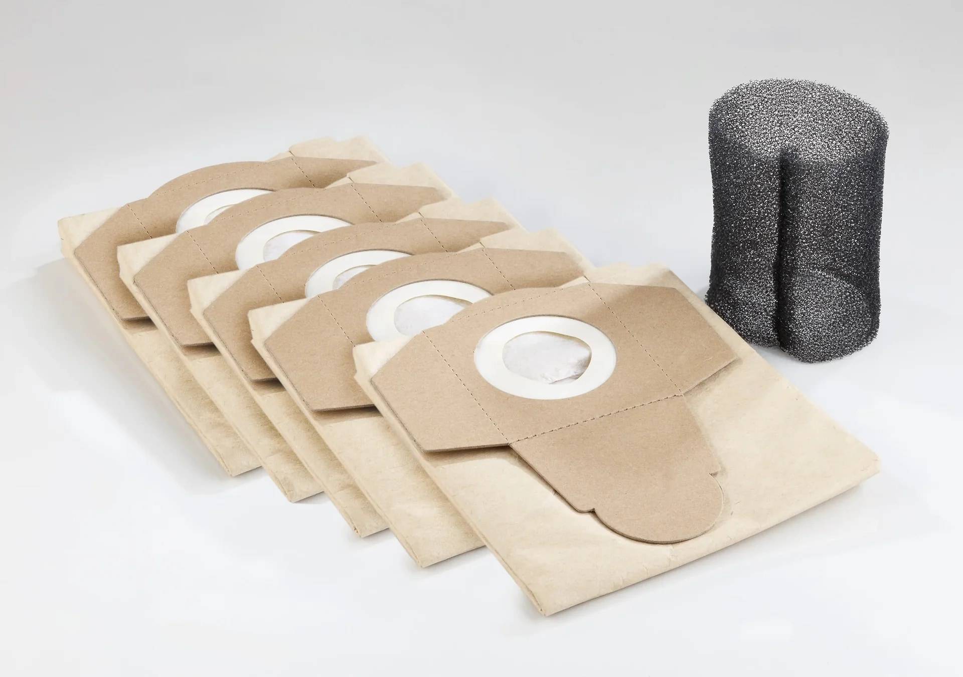 Stapel von beigen Staubsaugerpapier-Beuteln mit kreisförmigen Öffnungen neben einem schwarzen Schaumstofffilter auf weißem Hintergrund.