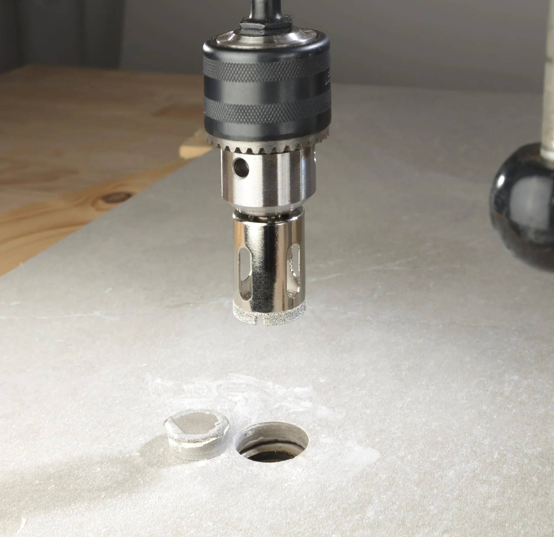 Nahaufnahme eines Bohrfutters und eines Bohrers über einem Metallblech mit zwei gebohrten Löchern und Metallspänen, die einen Bohrvorgang zeigen.