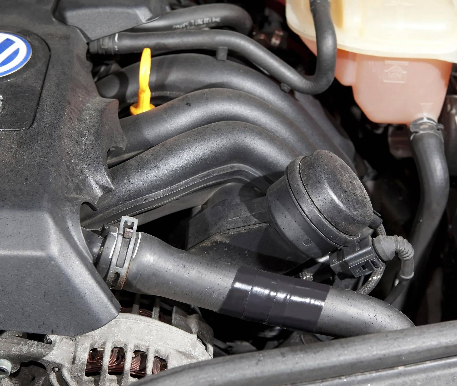 Nahaufnahme eines Motorraums eines Autos, die schwarze Ansaugschläuche, einen gelben Ölmessstab und einen Kühlmittelbehälter zeigt.