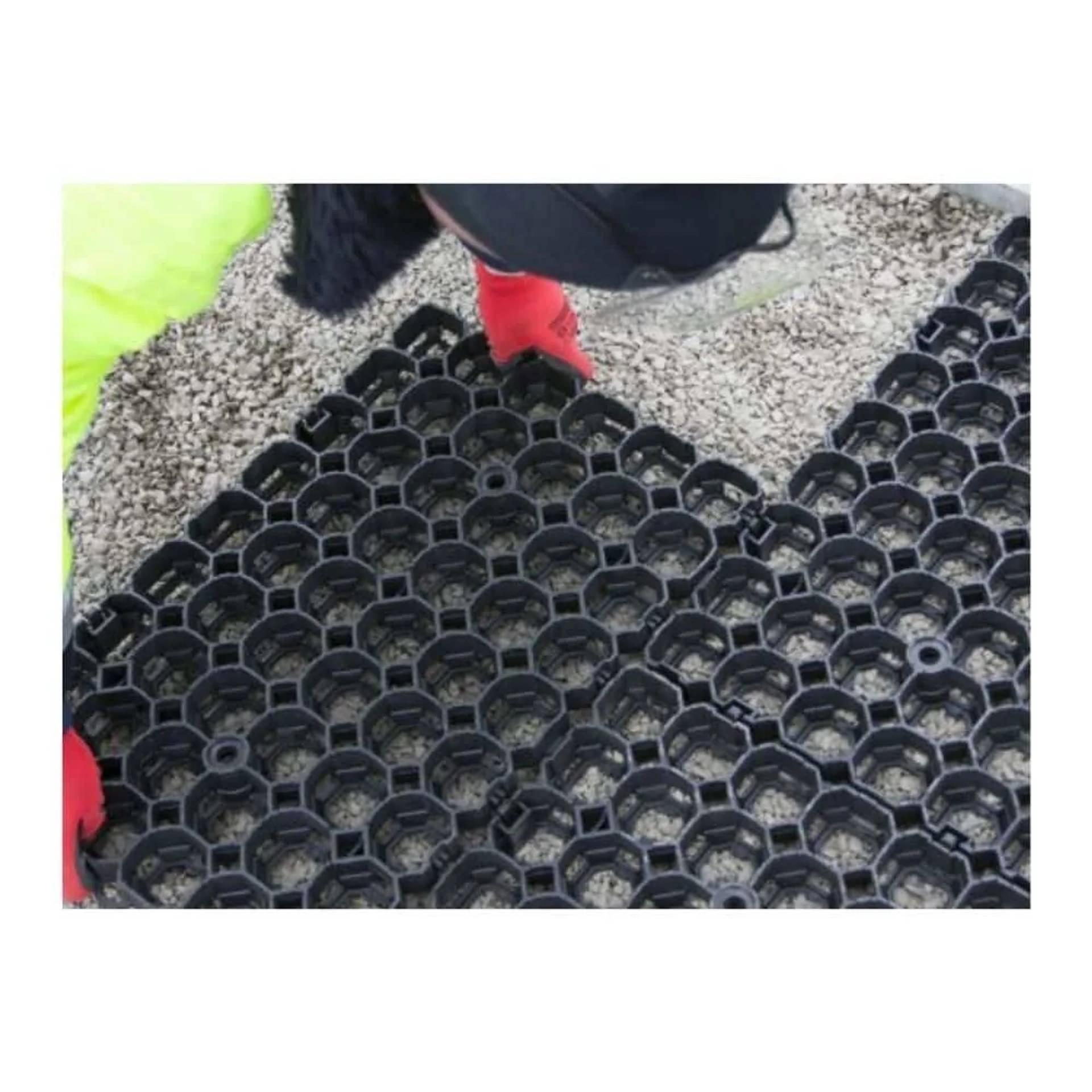 Arbeiter in roten Handschuhen verlegt eine schwarze sechseckige Kunststoffgittermatte auf Kies, wahrscheinlich für Bodenstabilisierung oder Drainage.