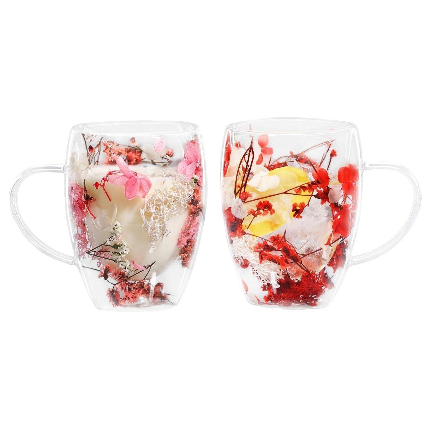 Zwei klare Glastassen mit Henkeln, jeweils mit eingearbeiteten roten, rosa und gelben Blumenmustern auf weißem Grund verziert.