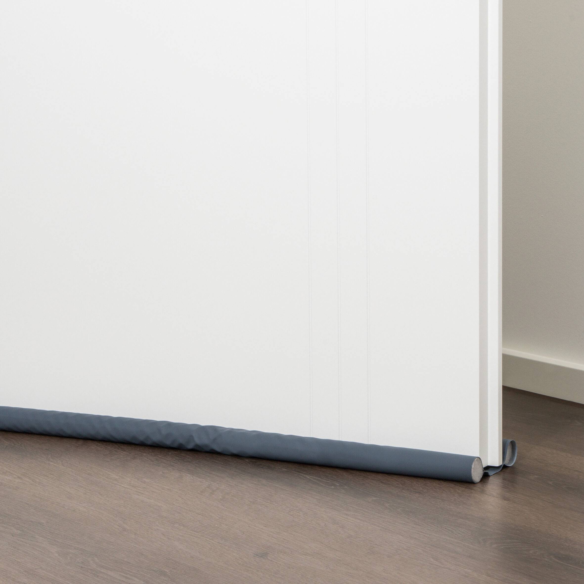 Unterkante eines weißen Panels oder Bildschirms mit einem dunklen Zugluftstopper entlang des Bodens in einem Zimmer mit Holzfußboden.