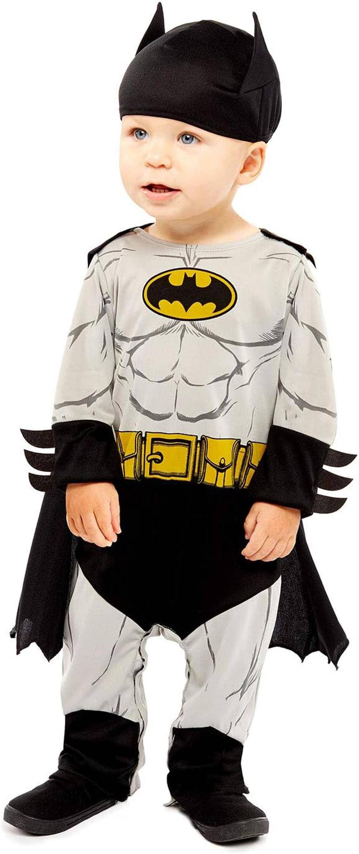 Kleinkind in einem Batman-Kostüm gekleidet mit schwarzem Umhang, Maske, Handschuhen, Stiefeln und gelbem Fledermaus-Logo auf der Brust, stehend vor einem weißen Hintergrund.