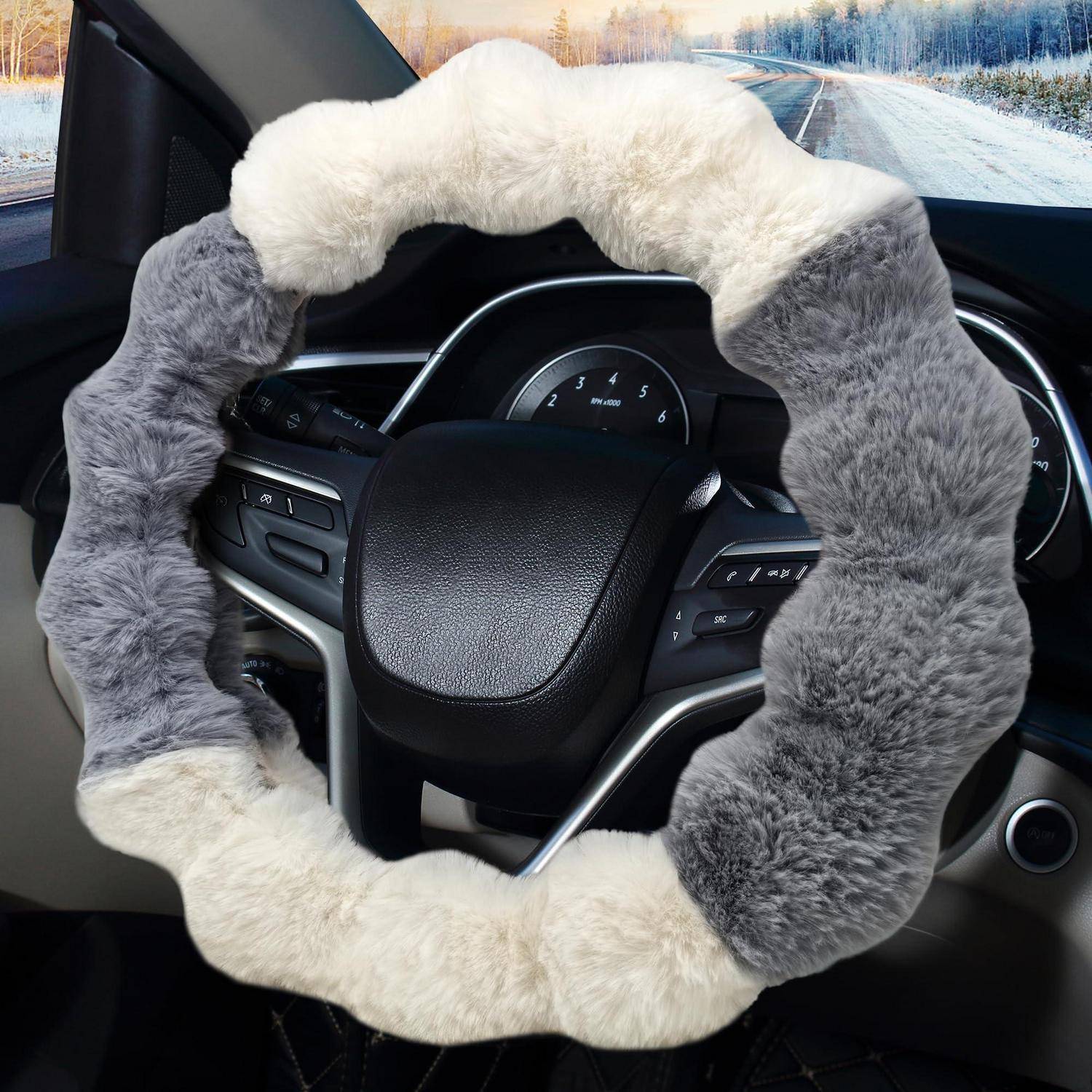 Ein flauschiger weiß-grauer Lenkradbezug auf einem Autolenkrad, mit Armaturenbrett und verschneiter Straße sichtbar durch die Windschutzscheibe.