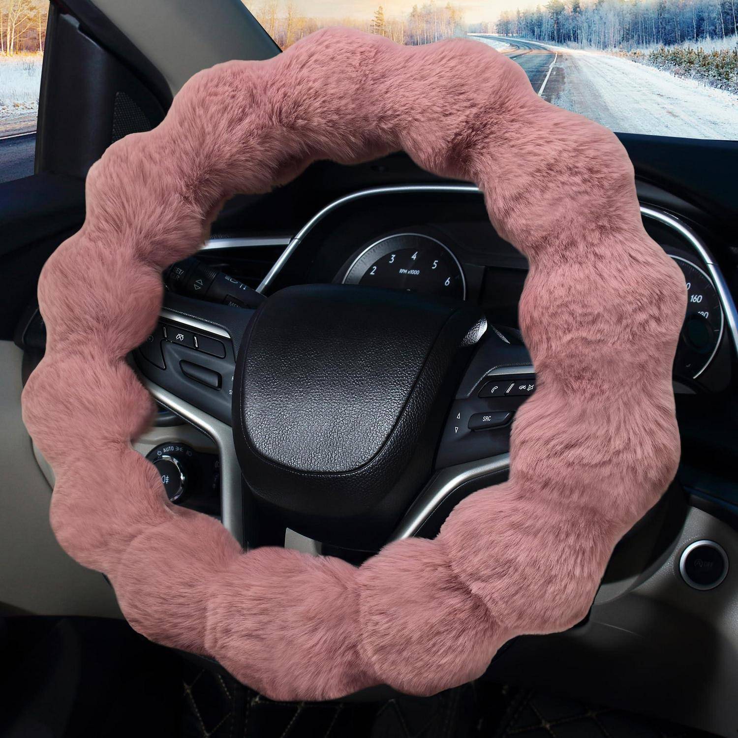 Ein rosa flauschiger Lenkradbezug auf einem Armaturenbrett eines Autos, mit einer verschneiten Straße, die durch die Windschutzscheibe sichtbar ist.