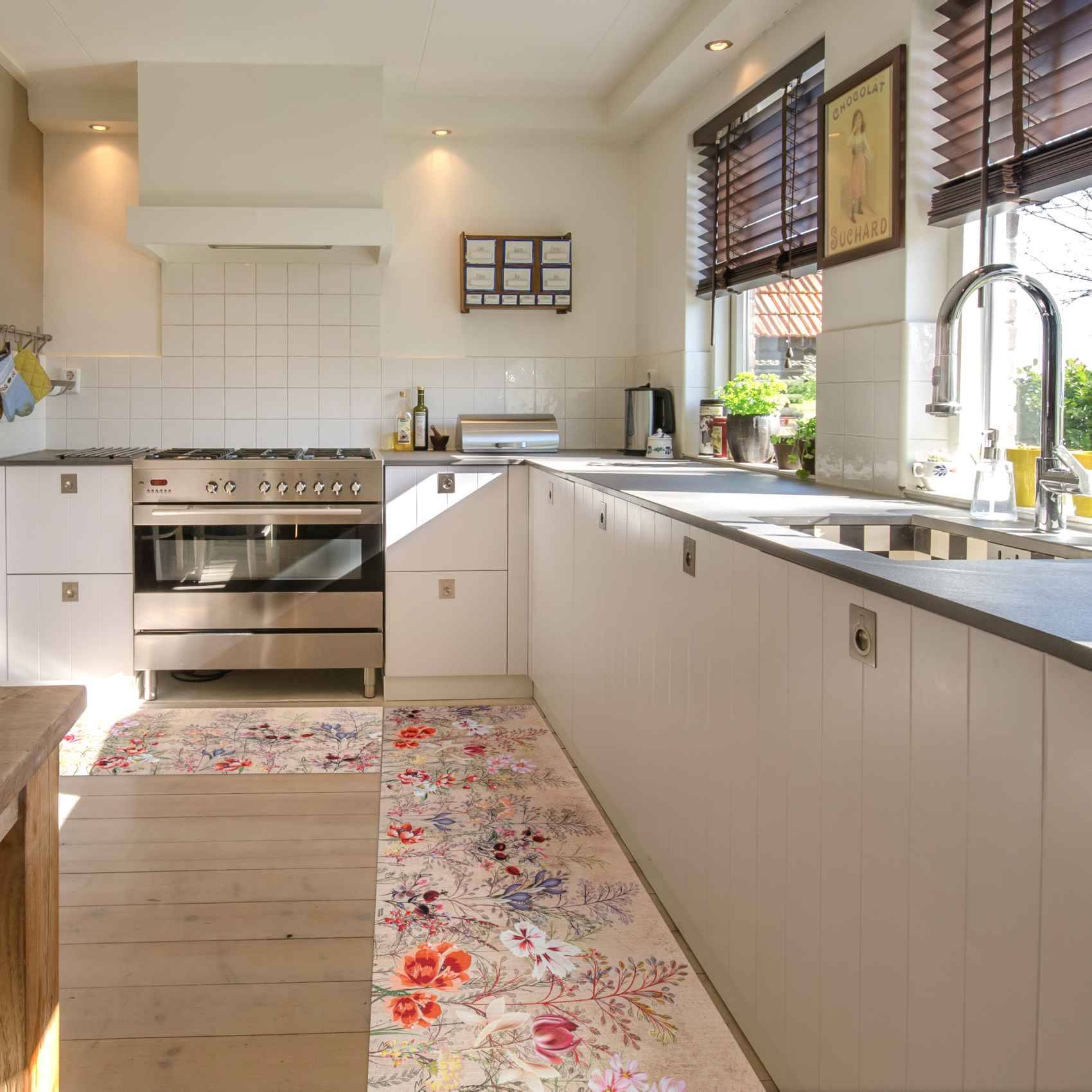 Helle moderne Küche mit weißen Schränken, Edelstahlherd, langer Arbeitsplatte mit Spüle neben Fenstern und einem Blumenmuster-Läufer.