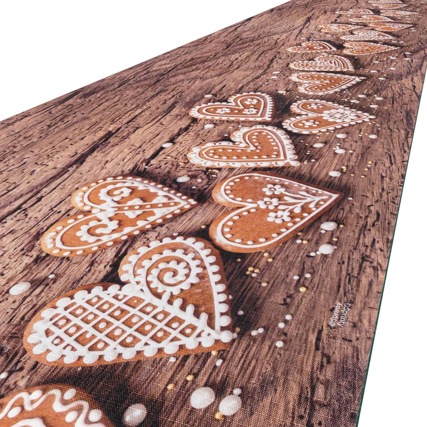 Nahaufnahme eines Holzbretts, das mit einer diagonalen Reihe aus orange-weiß gefärbten herzförmigen Lebkuchenplätzchen und verstreuten Zuckerglasur-Punkten verziert ist.