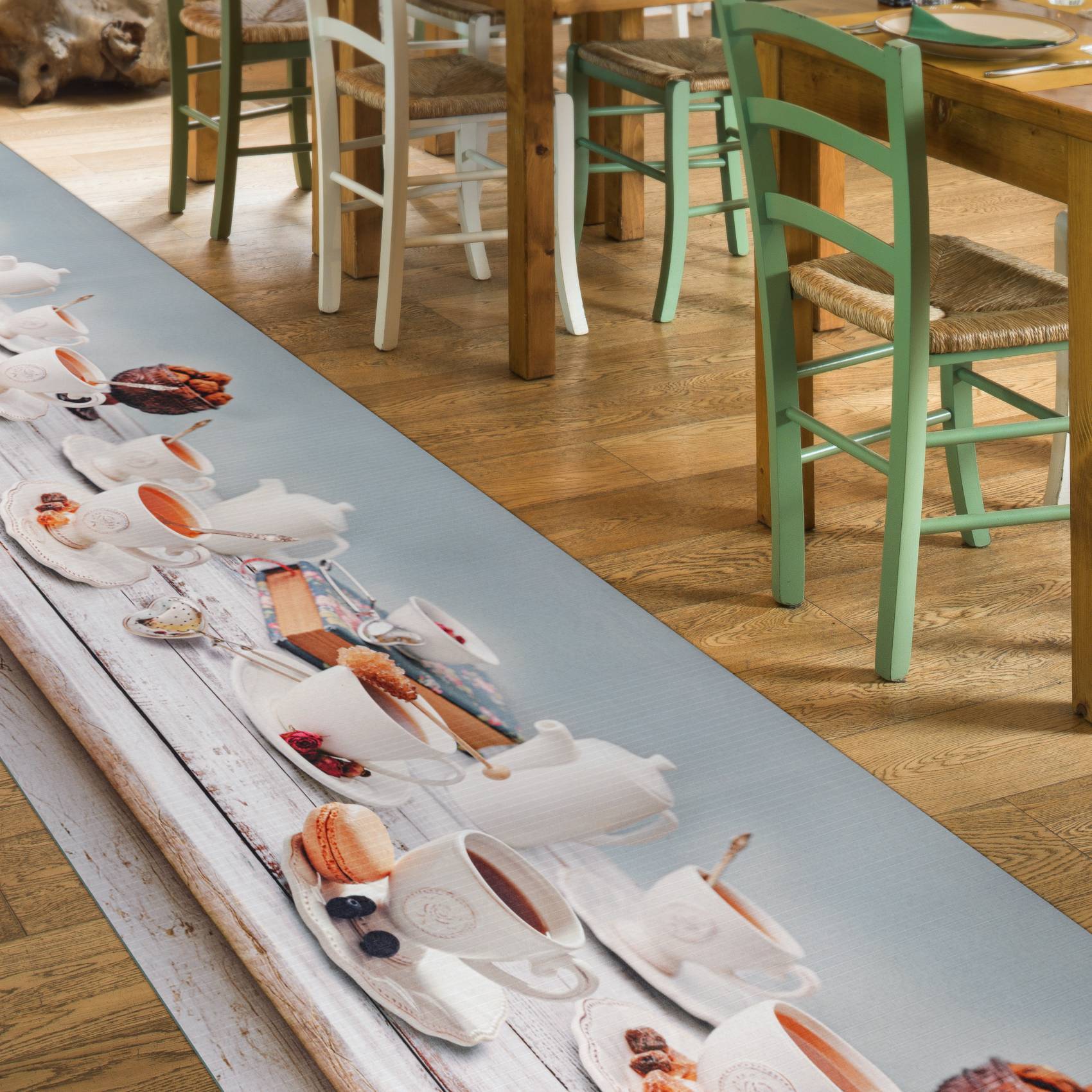 Café-Tisch mit einem langen bedruckten Tischläufer, der weiße Kaffeetassen, Untertassen und Gebäck auf einer Holzoberfläche zeigt.