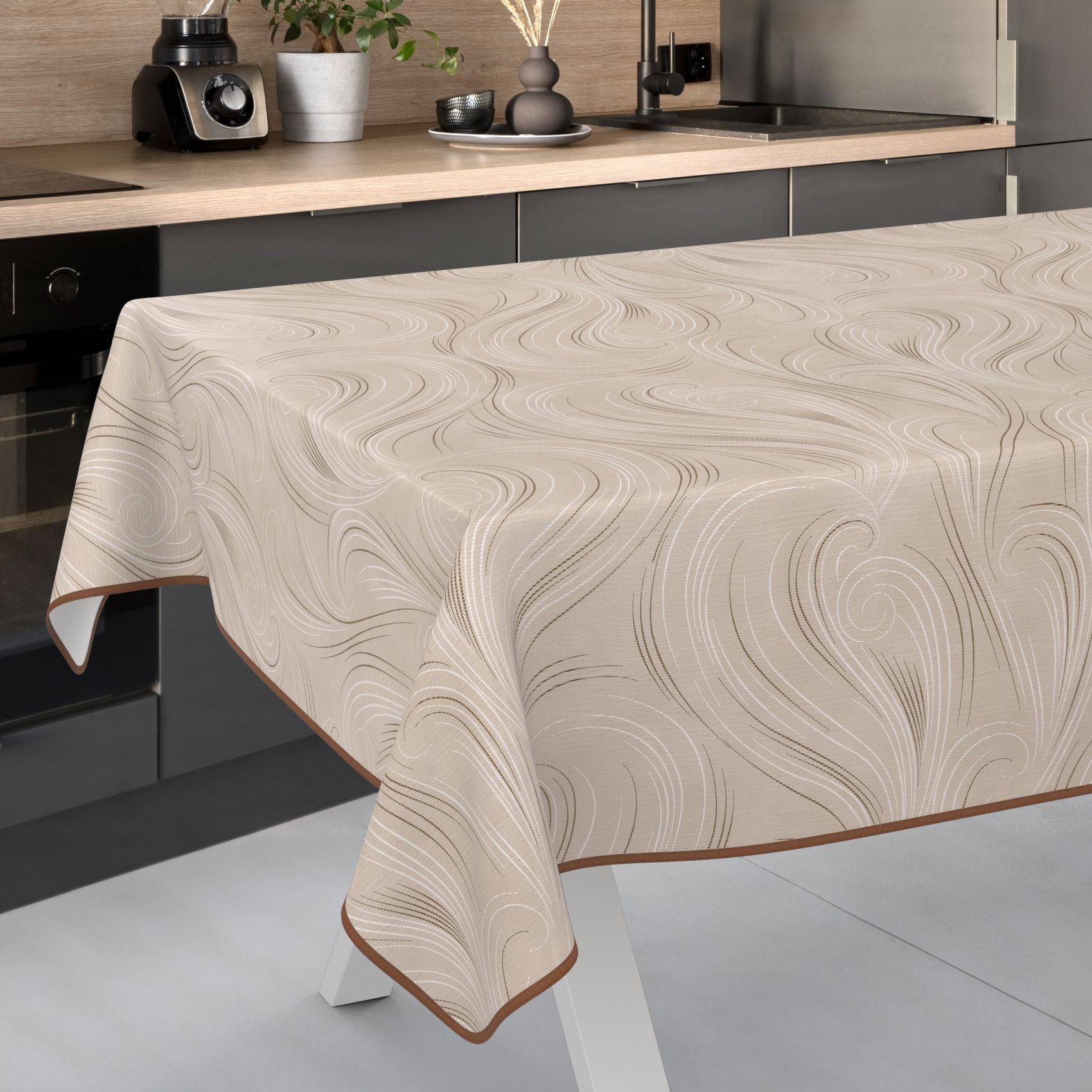 Beigefarbige gemusterte Tischdecke, die über einen Tisch in einer modernen Küche drapiert ist, mit einer Kaffeemaschine und Arbeitsplattendekoration im Hintergrund.