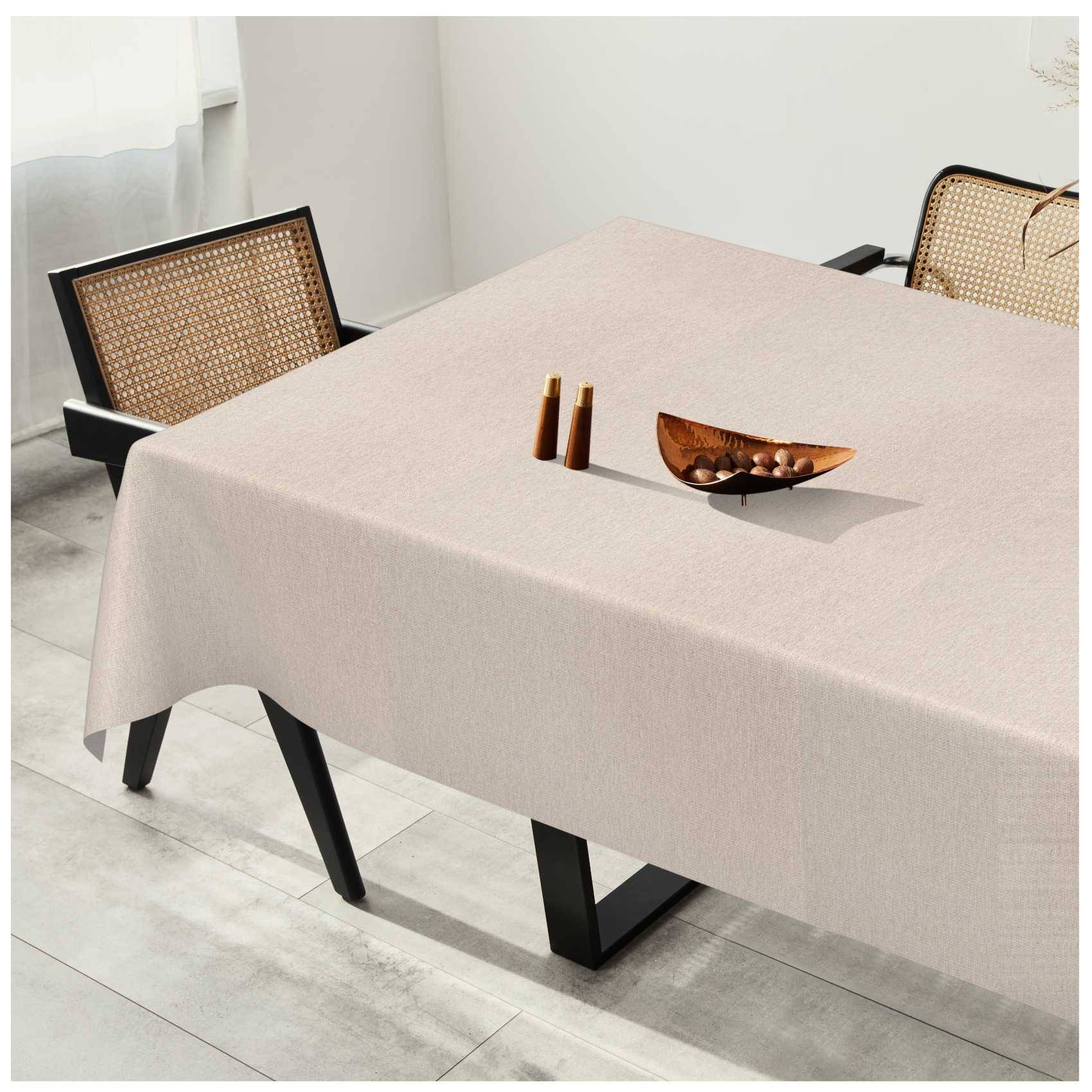 Minimalistischer Esstisch mit beigefarbener Tischdecke, zwei Stühlen mit Rohrgeflecht-Rückenlehne und einer Holzschüssel mit kleinen Flaschen in einem hellen Raum.