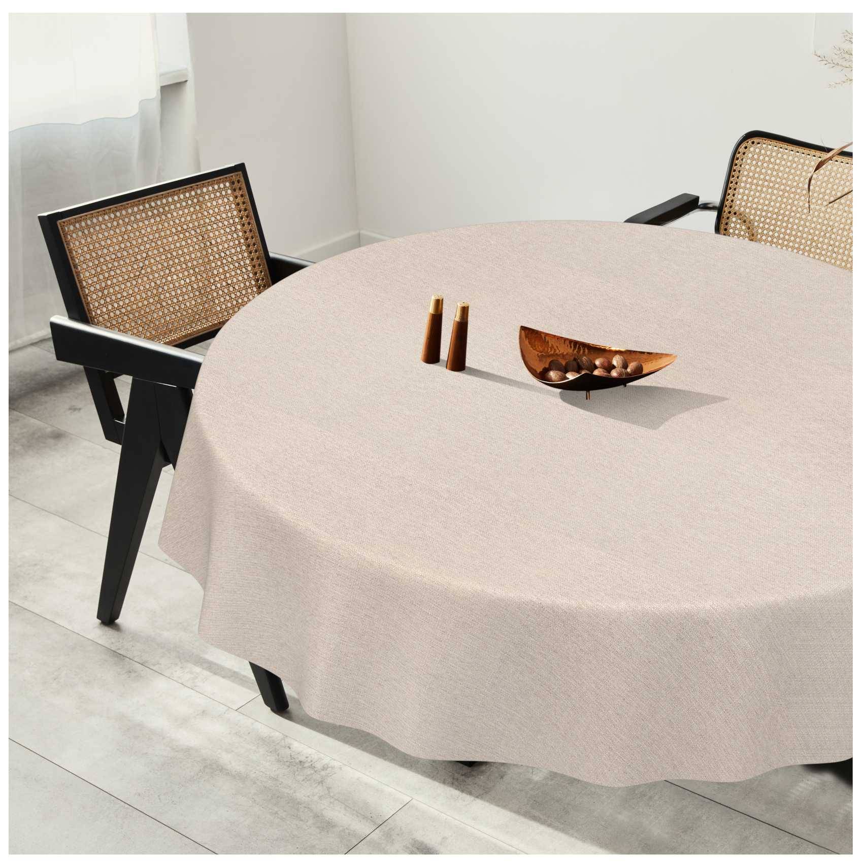 Runder Esstisch mit beigefarbiger Tischdecke und zwei Stühlen aus Rattan in einem hellen, minimalistischen Raum, mit kleinen Holzdekorationen auf dem Tisch.