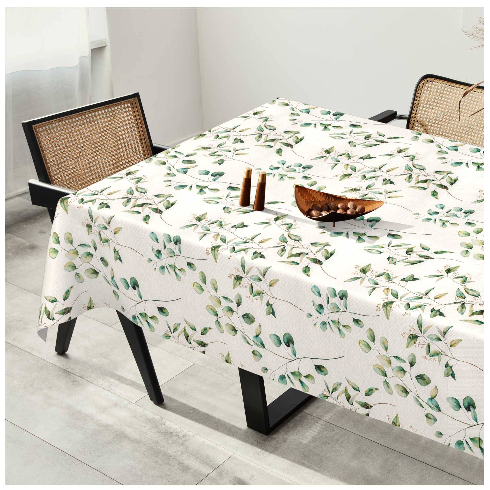 Esstisch mit einer weißen Tischdecke mit Blattmuster, zwei Stühlen mit Rohrgeflecht-Rückenlehne und einer kleinen Holzschale sowie Kerzenhaltern darauf.