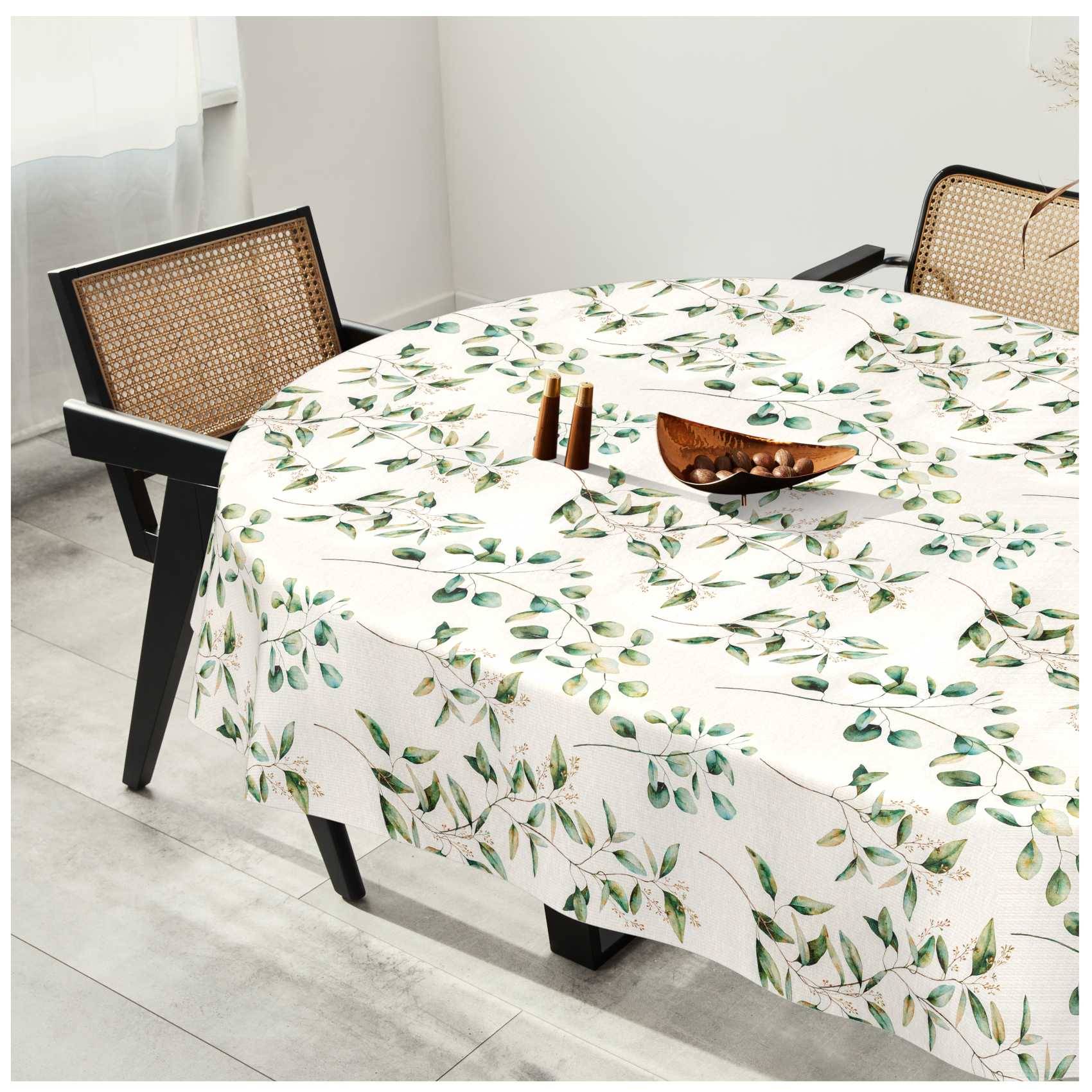 Runder Esstisch mit weißer Blumentischdecke, Holzschüssel als Tischdekoration in der Mitte und zwei Stühle mit gewebtem Rückenlehnen in einem hellen Raum.