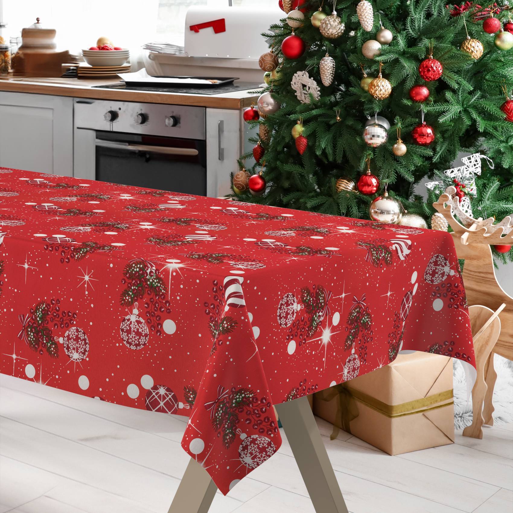 Festliche Küche mit einer rot gemusterten Weihnachtstischdecke auf einem Esstisch neben einem geschmückten Baum, Rentieren und verpackten Geschenkboxen.