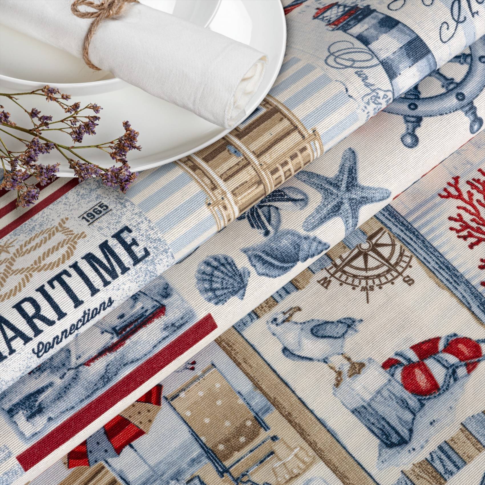 Marinethemen-Baumwollstoff zum Aufrollen mit Muschel-, Seestern-, Leuchtturm-, Anker- und Seemanndrucken in Blau, Rot und Beige.