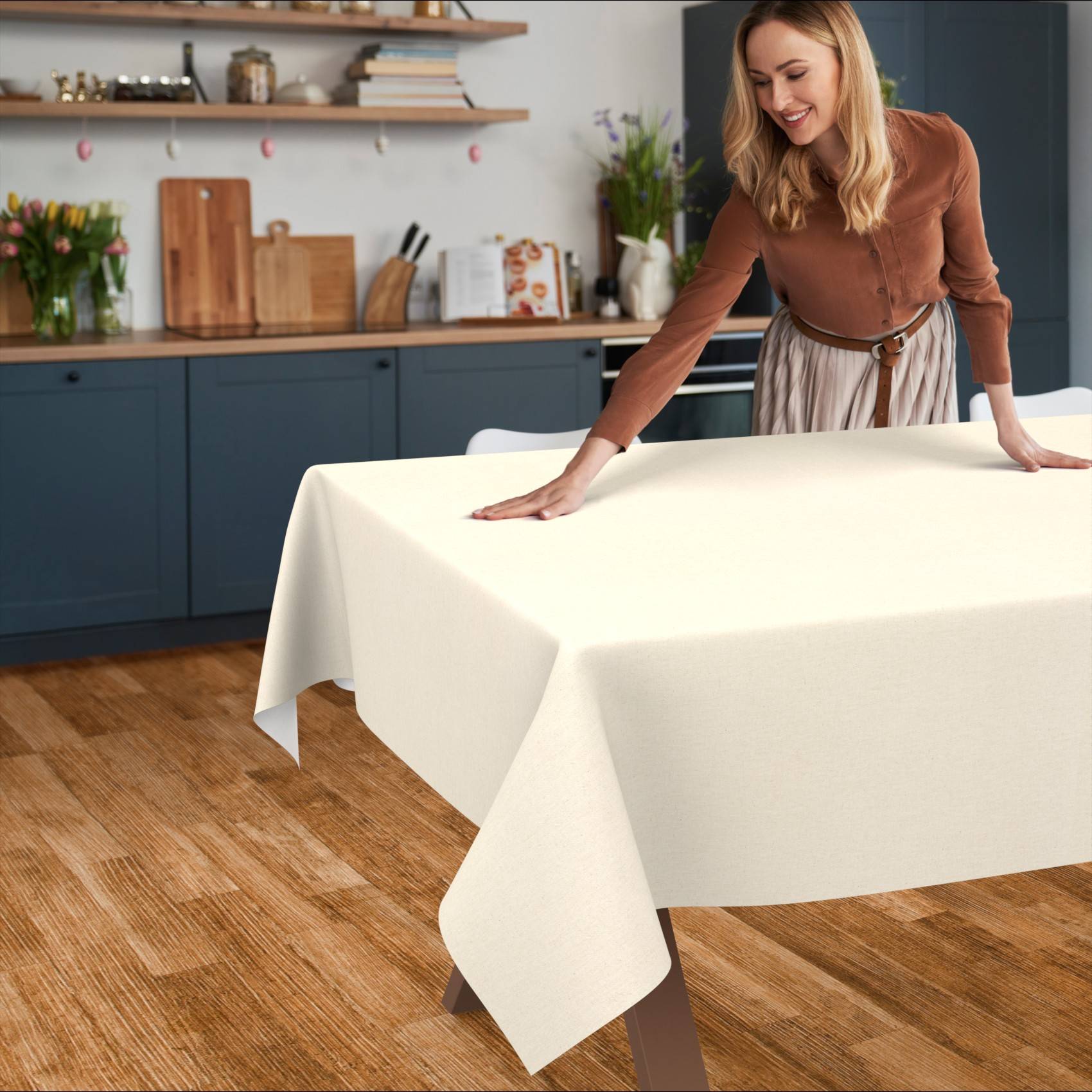 Eine Frau glättet eine cremefarbene Tischdecke über einen Esstisch in einer Küche.
