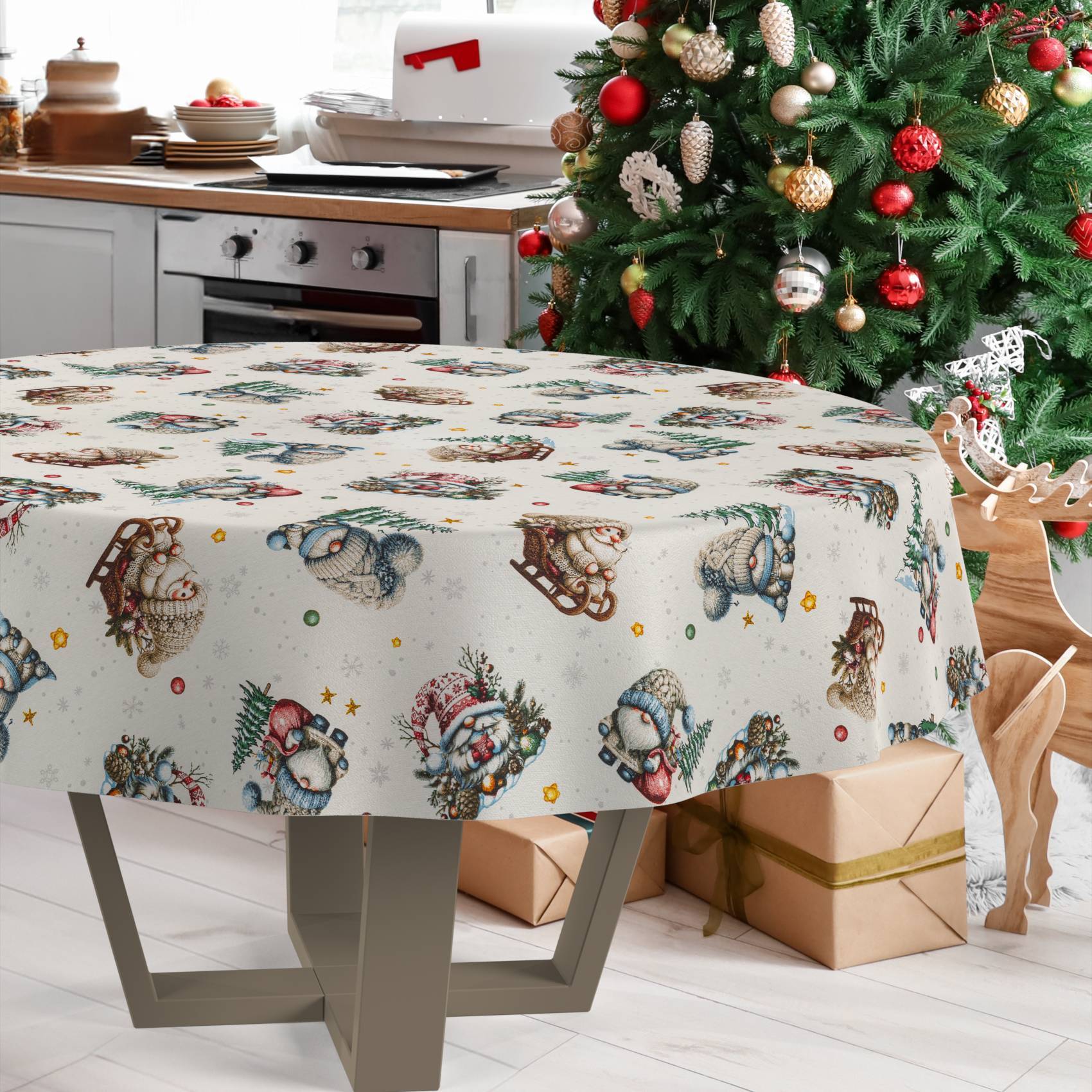 Festlicher Esstisch mit Weihnachtsmuster-Tischdecke neben verziertem Baum, Geschenken und einer Rentierdekoration in einer Küche.