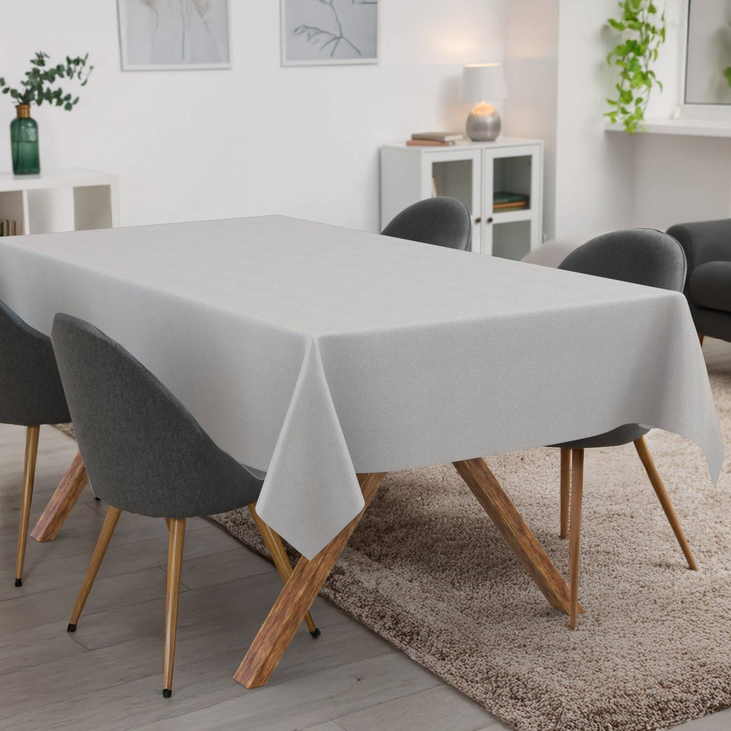 Esstisch mit einer hellgrauen Tischdecke in einem modernen Wohnzimmer, umgeben von dunklen Stühlen und einem Teppich.