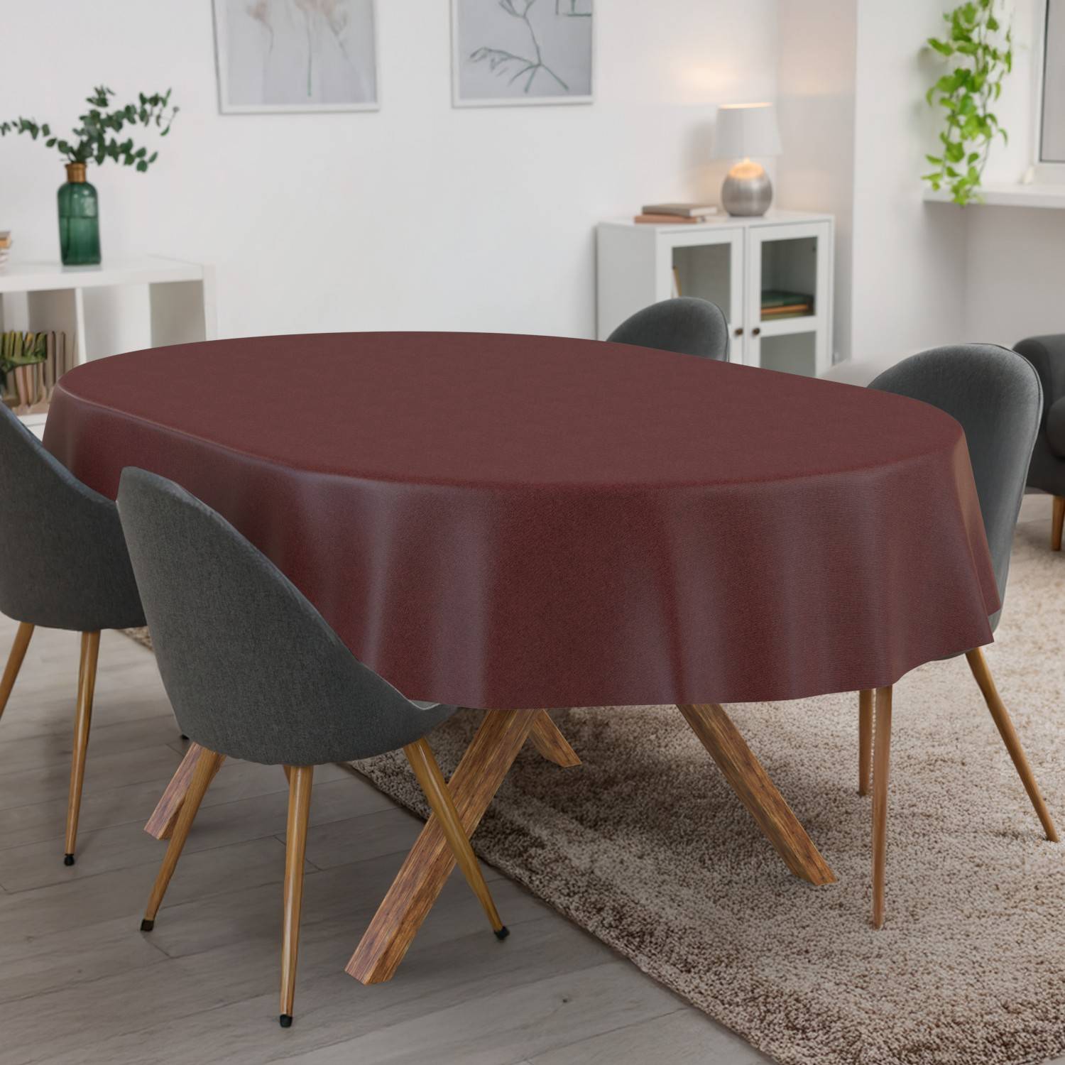 Ein Esszimmer mit einem ovalen Tisch, der mit einer dunkelroten Tischdecke bedeckt ist, umgeben von grauen Stühlen auf einem Teppich, mit Regalen und Pflanzen im Hintergrund.