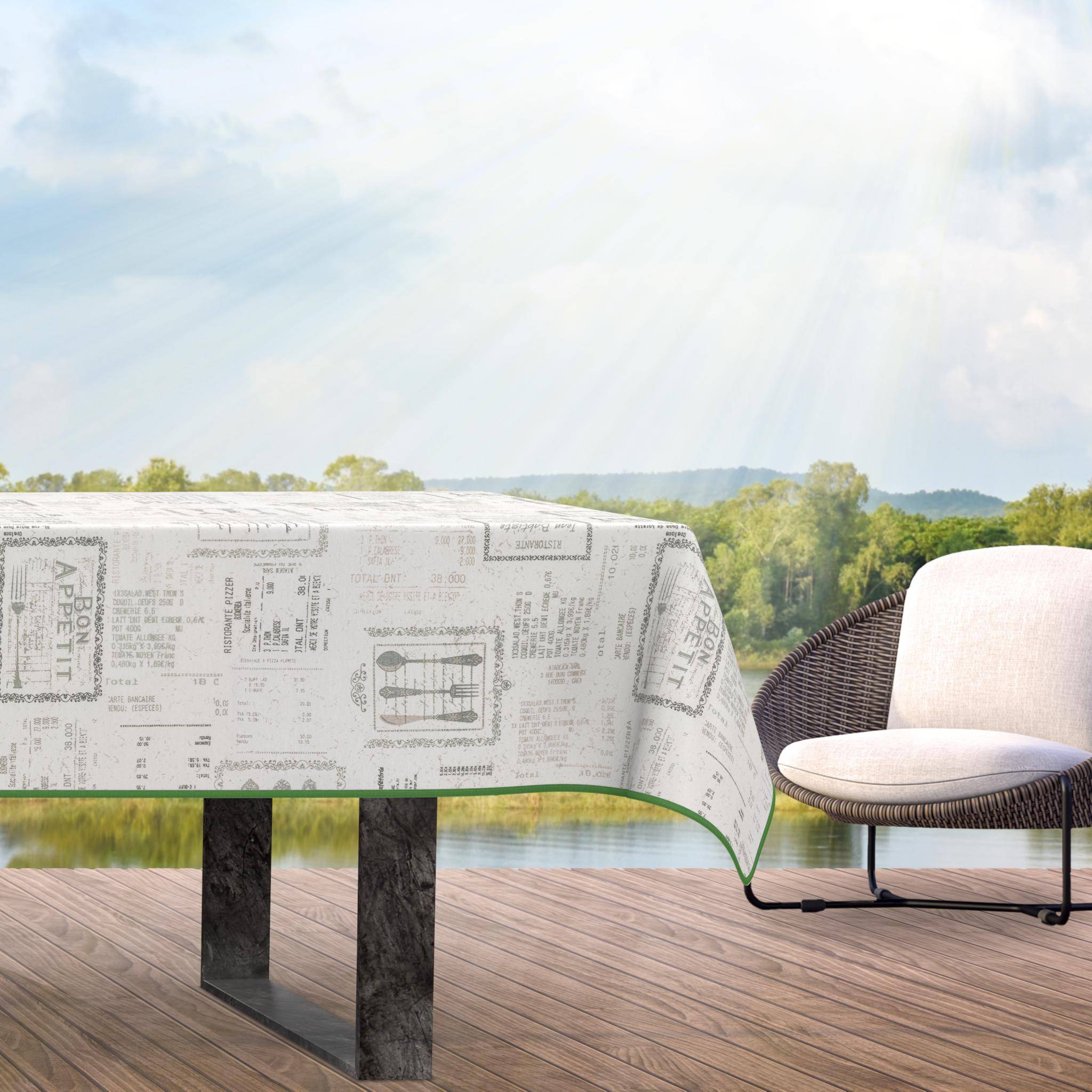 Außenbereich einer Terrasse mit einem Tisch, bedeckt mit einer Tischdecke im Zeitungsdruck-Design, und einem Korbstuhl daneben, mit Blick auf Bäume und entfernte Hügel im Sonnenlicht.