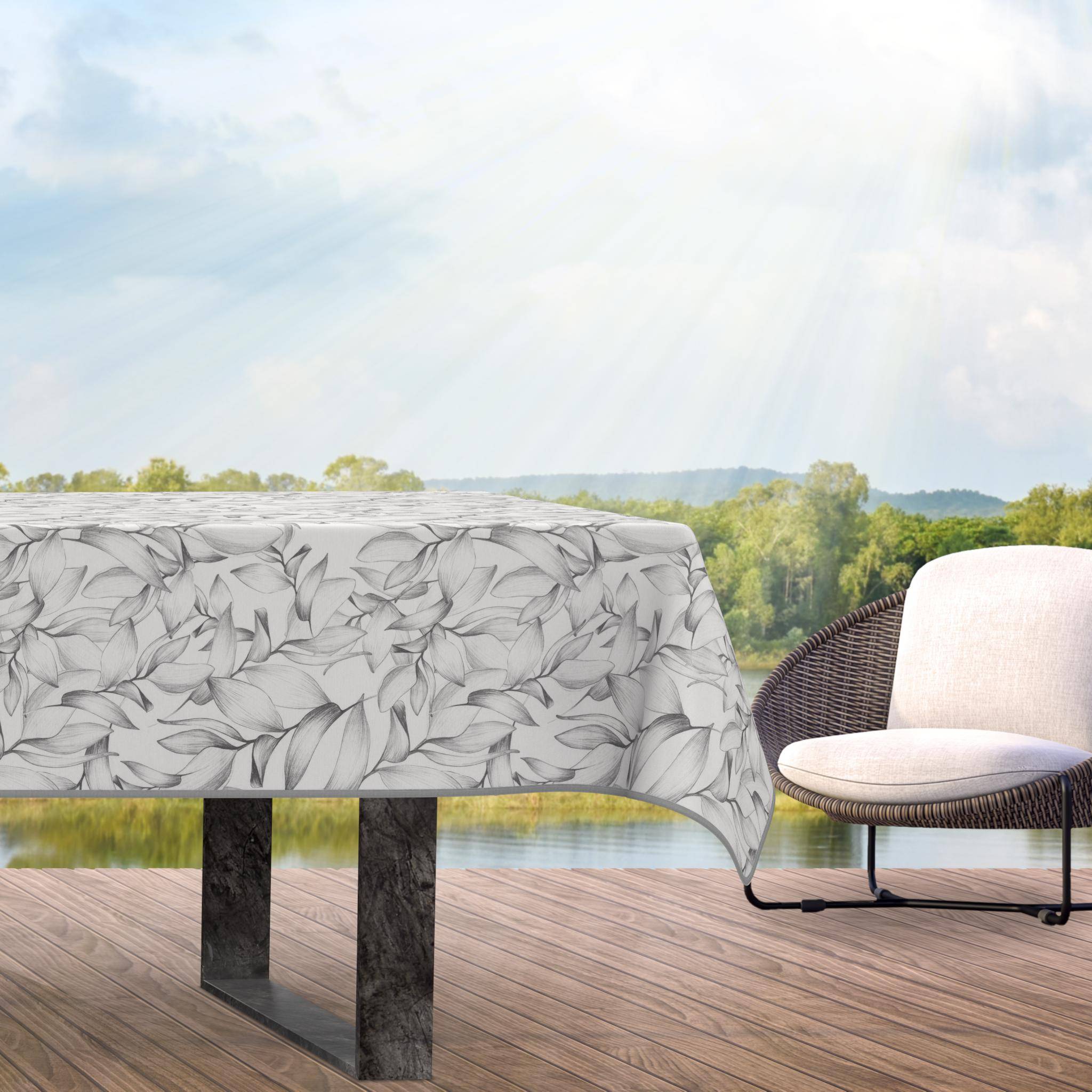 Outdoor-Esstisch mit einer blattgemusterten Tischdecke neben einem gepolsterten Stuhl auf einer Terrasse mit Blick auf eine malerische Landschaft.