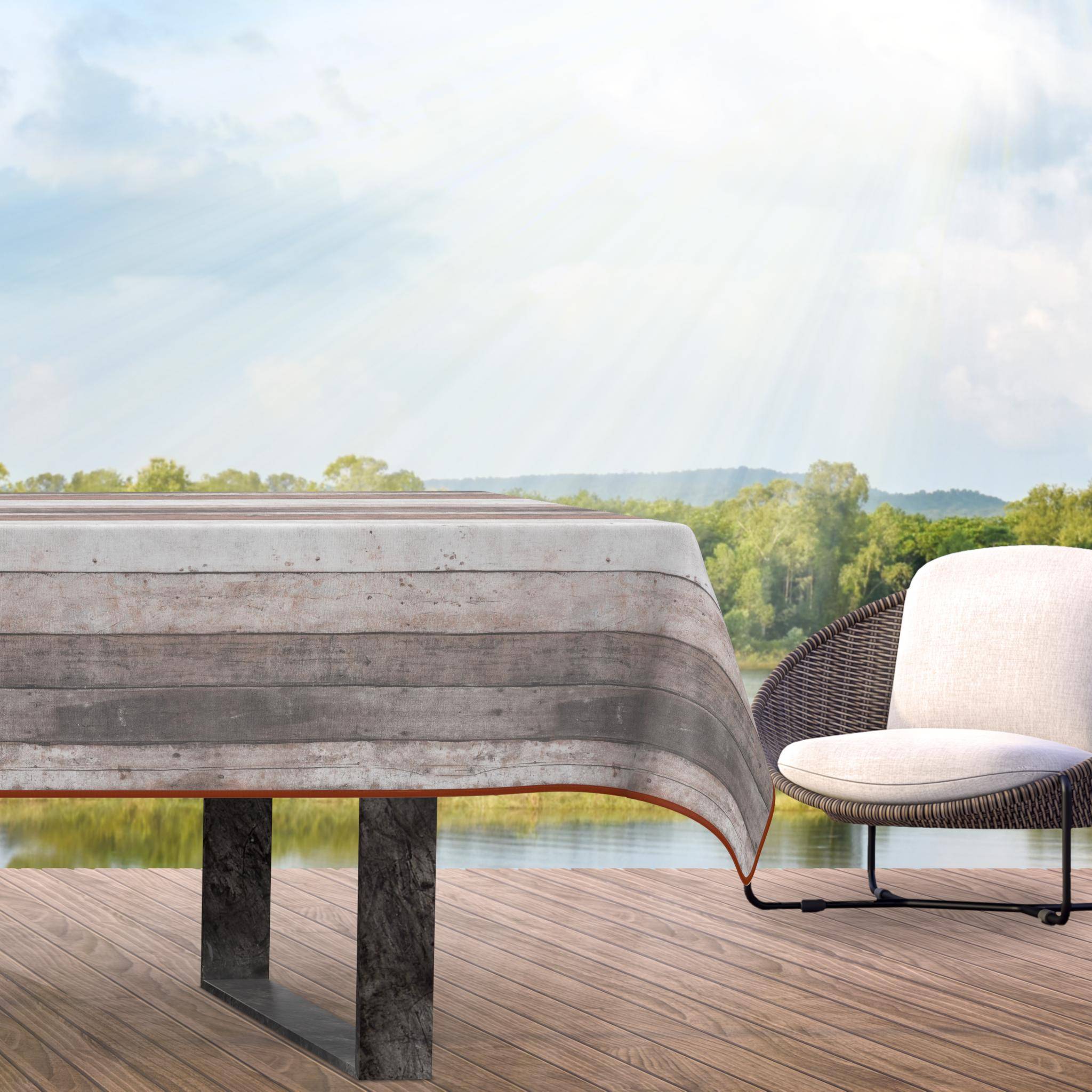 Esstisch für die Terrasse im Freien mit gestreifter Tischdecke neben einem gepolsterten Korbstuhl, mit Blick auf einen See und Bäume unter hellem Sonnenlicht.
