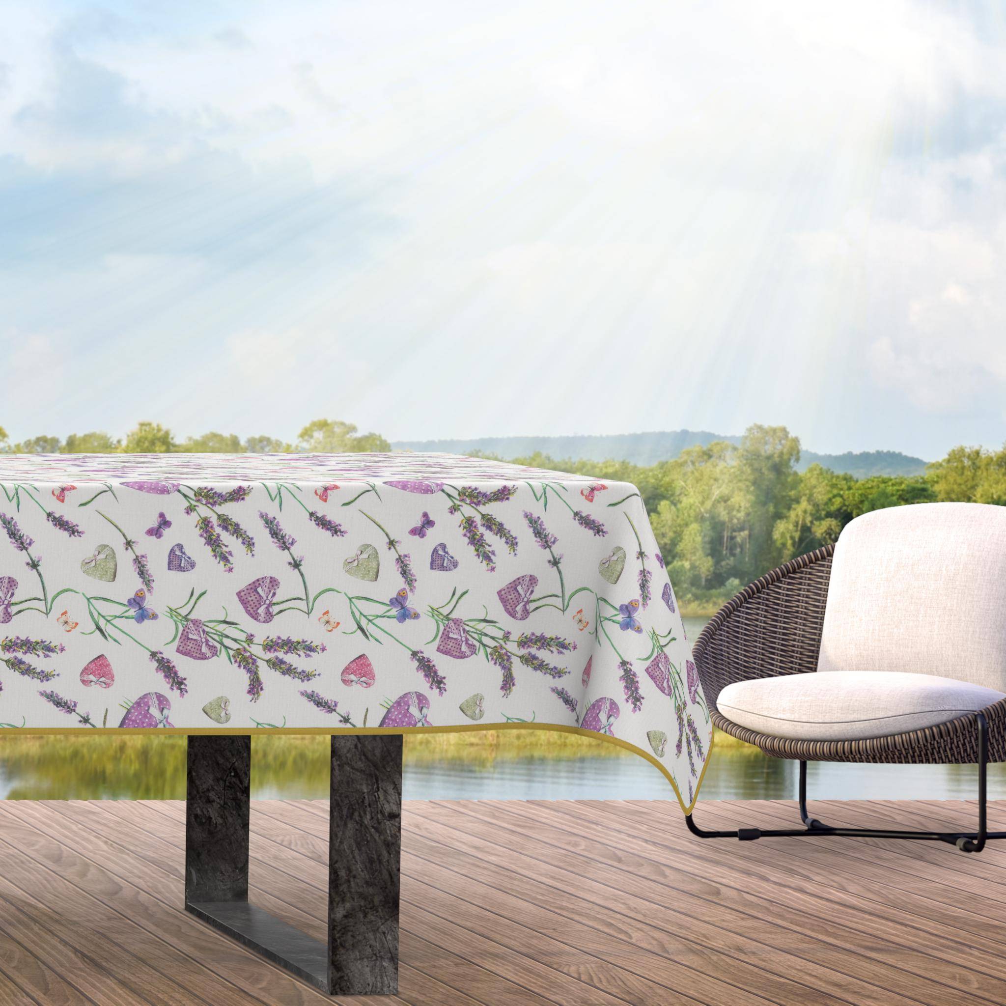 Tisch mit schmetterlingsmustertem Tischtuch und gepolstertem Stuhl auf einer Holzterrasse mit Blick auf einen See und Hügel unter heller Sonneneinstrahlung.