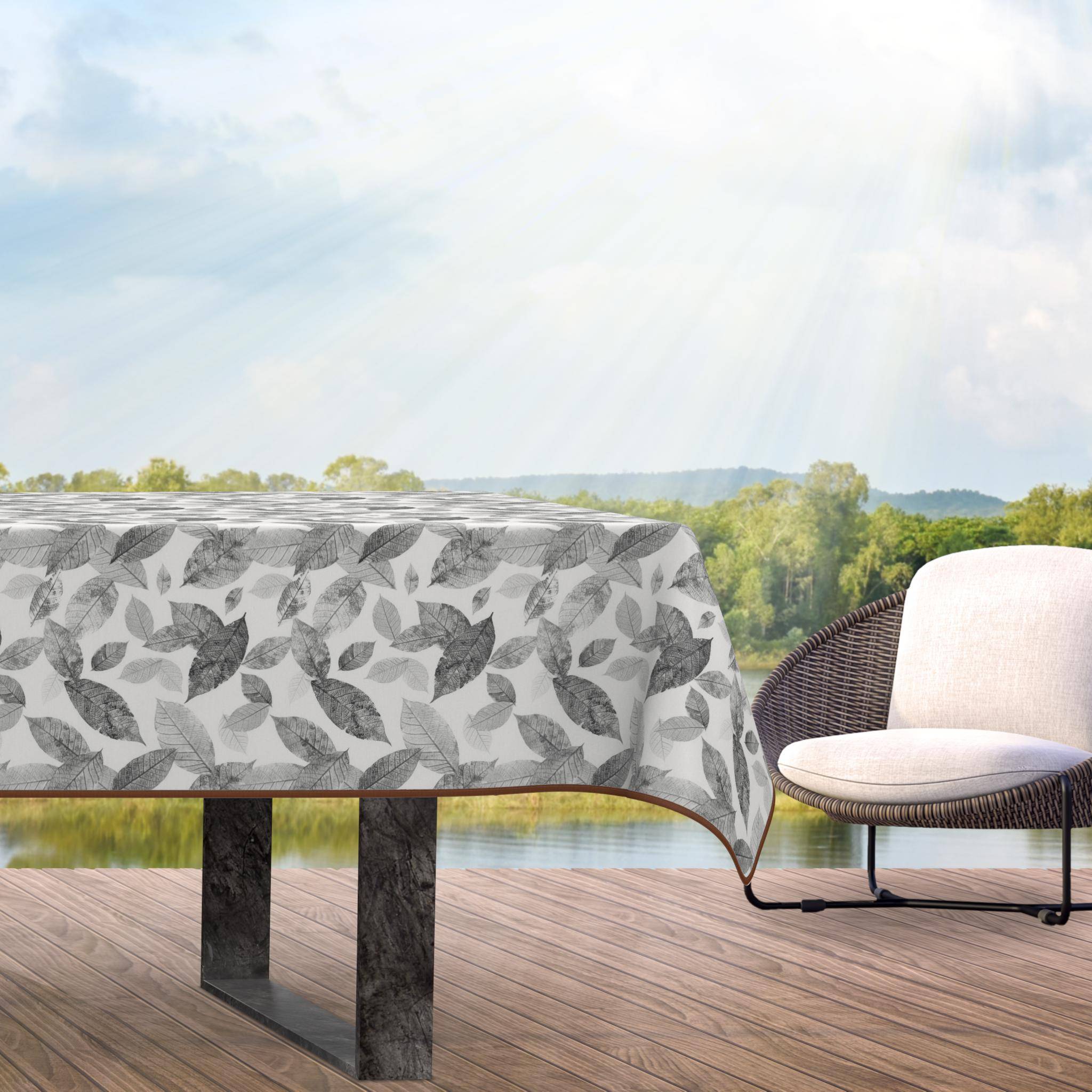 Outdoor-Terrassentisch mit blattgemusterter Tischdecke und einem Stuhl daneben, mit Blick auf einen See und Bäume in heller Sonneneinstrahlung.