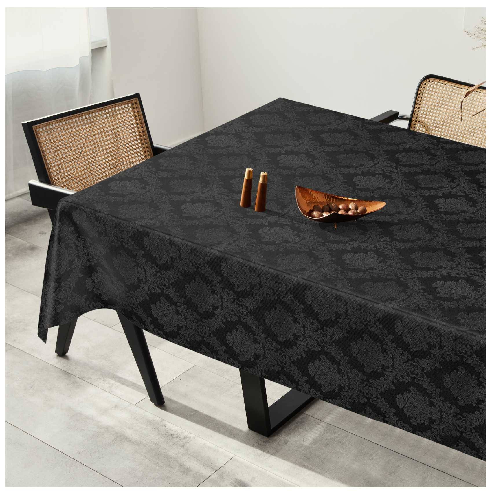 Schwarze gemusterte Tischdecke auf einem Esstisch mit zwei Stühlen mit Rohrgeflecht und einer kleinen dekorativen Schüssel in der Mitte.