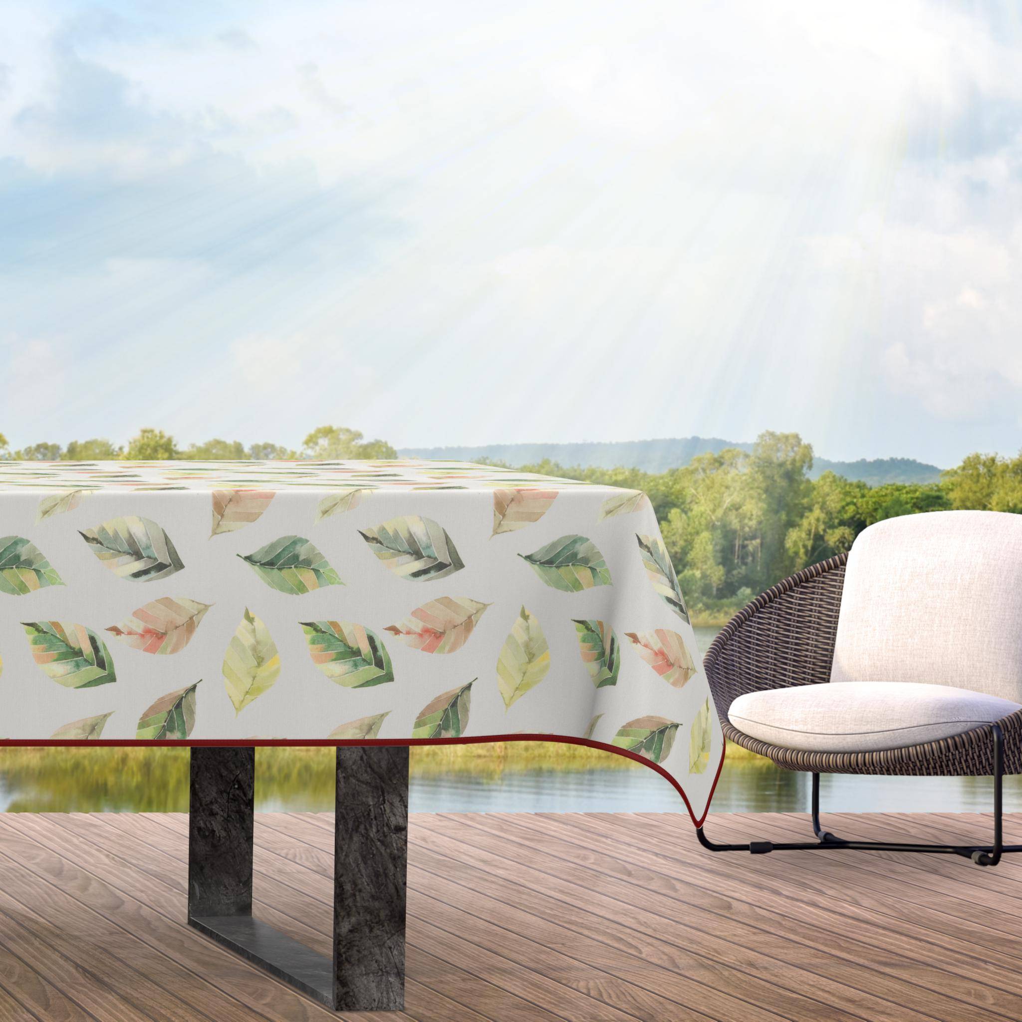 Outdoor-Essbereich mit blattgemustertem Tischtuch auf einem Tisch neben einem geflochtenen Stuhl auf einer Terrasse mit Blick auf Wasser und Hügel.