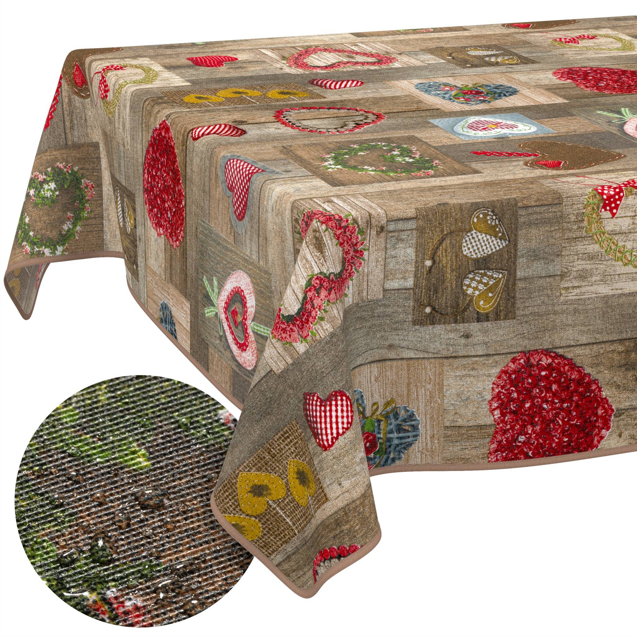 Rustikale Tischdecke mit Patchwork-ähnlichen Herz- und Blumenmotiven in Rot, Rosa und Gold auf holzstrukturiertem Hintergrund; die Ausschnittsvergrößerung zeigt gewebte Stoffstruktur.