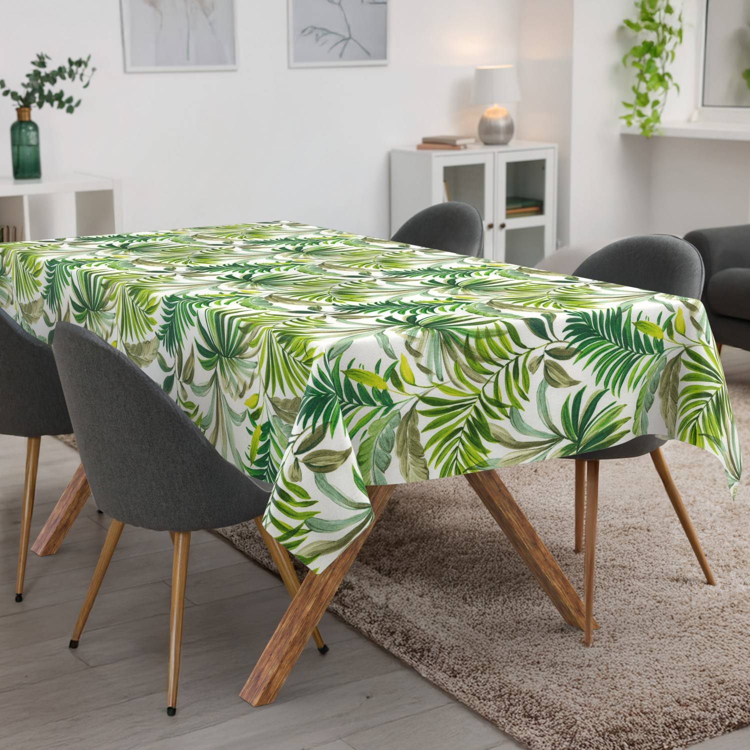 Esstisch mit einer grünen Tischdecke mit tropischem Blattmuster in einem modernen Wohnzimmer mit grauen Stühlen und einem Teppich.
