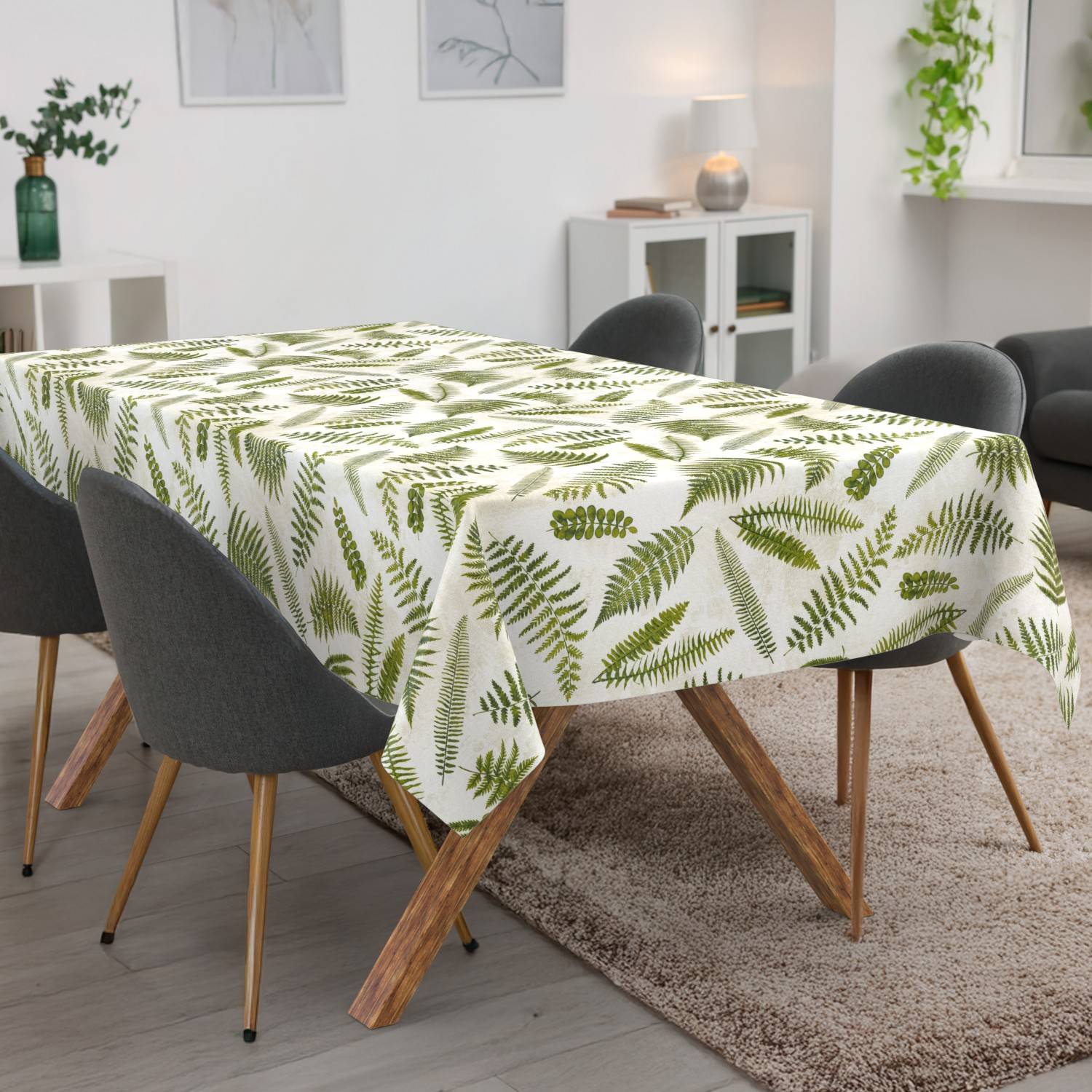 Esstisch mit einer weißen Tischdecke bedruckt mit grünen Farnblättern, umgeben von dunkelgrauen Stühlen in einem hellen modernen Raum.