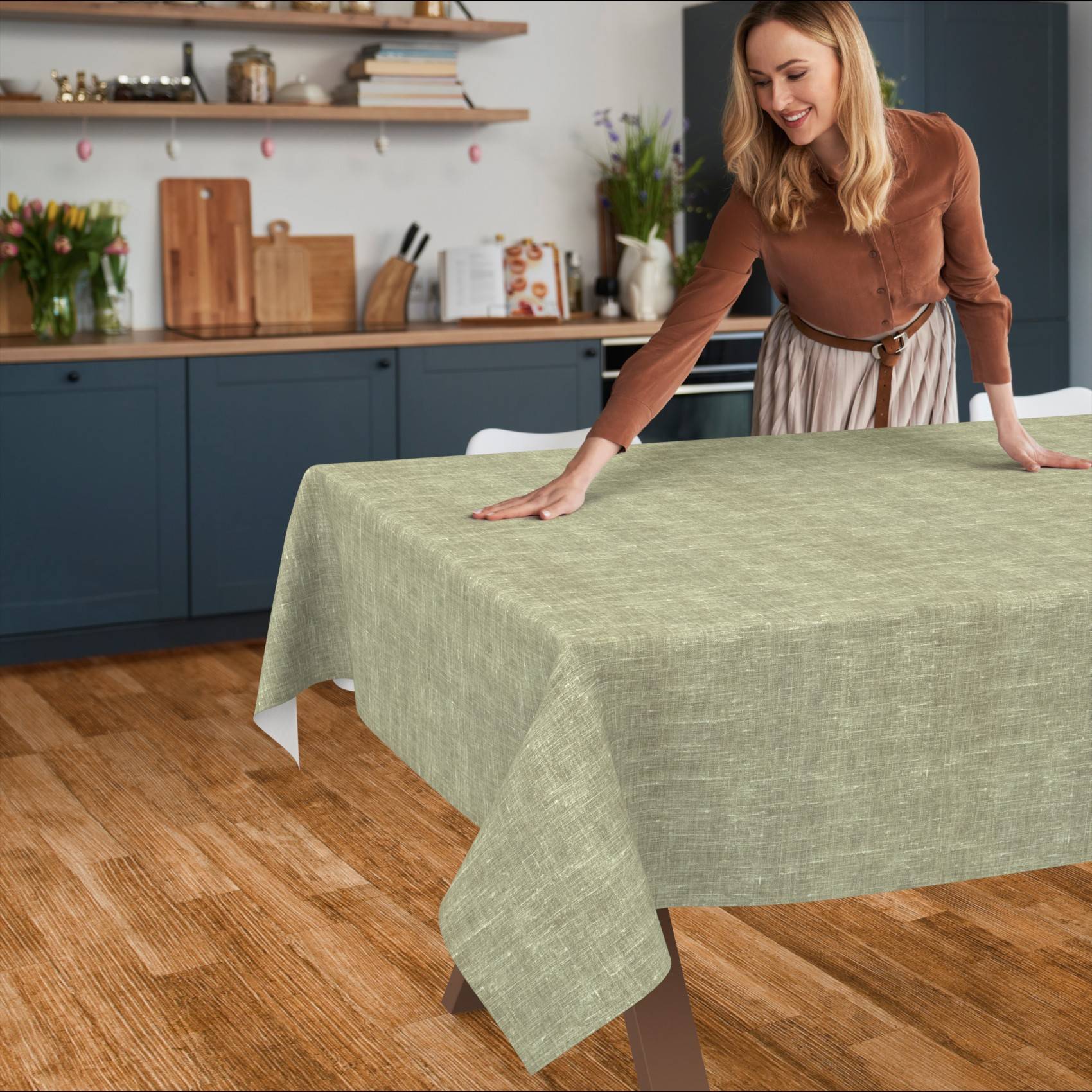 Eine Frau glättet eine hellgrüne Tischdecke über einen Esstisch in einer Küche.