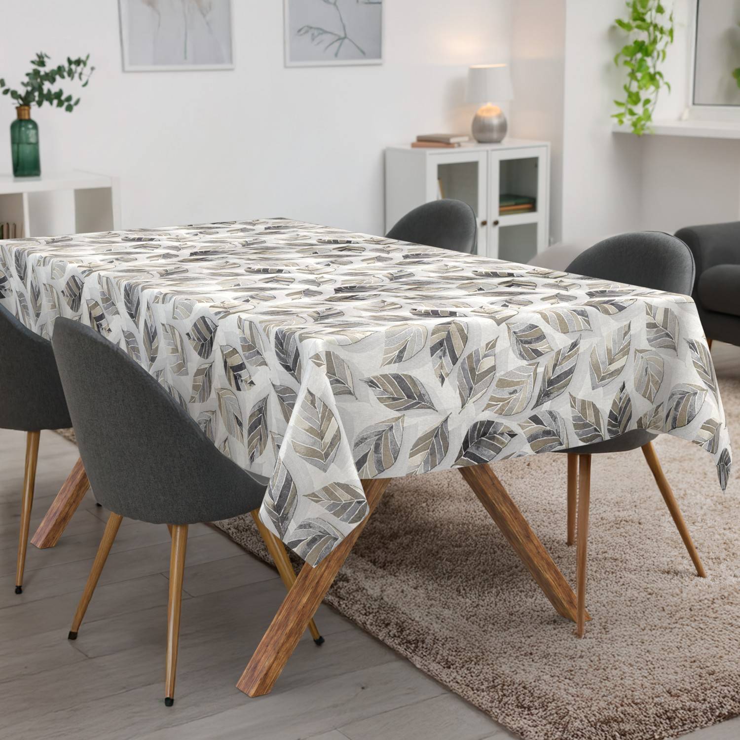 Esstisch mit blattgemusterter Tischdecke in einem hellen modernen Wohnzimmer, umgeben von dunklen Stühlen und einem Teppich.
