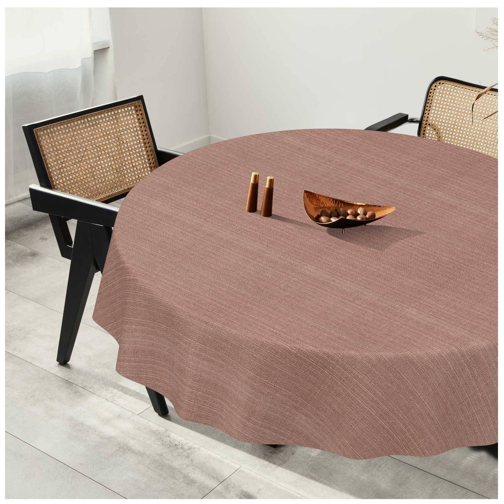 Runder Esstisch mit braunem Tuch, zwei Rattanstühle und eine kleine Holzschale als Tischdekoration in einem hellen Raum.