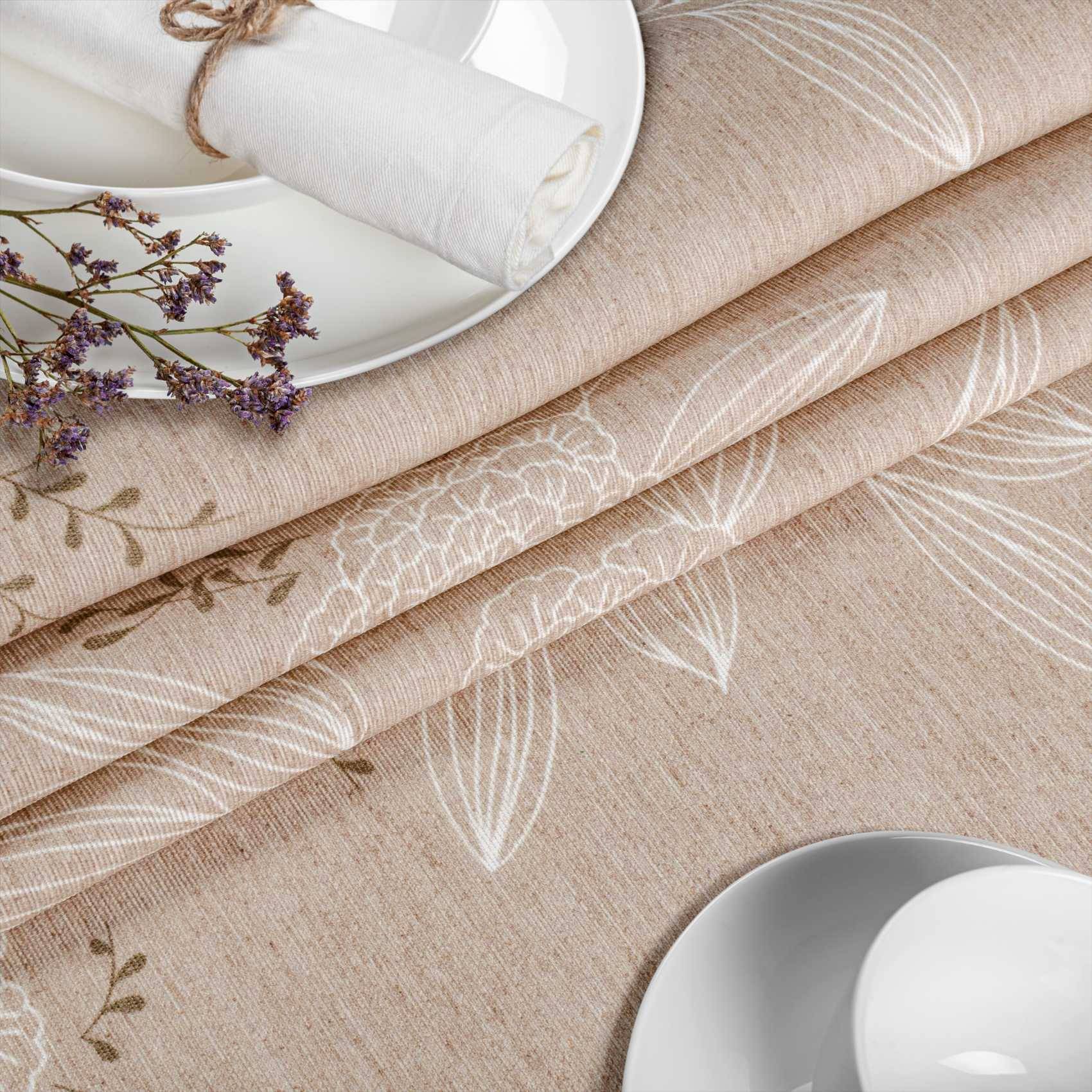 Nahaufnahme von gefalteten beige- und crèmefarbenen Leinenstoffen mit Blumendruck, arrangiert neben weißen Tellern und getrockneten Blumen auf einem Tisch.