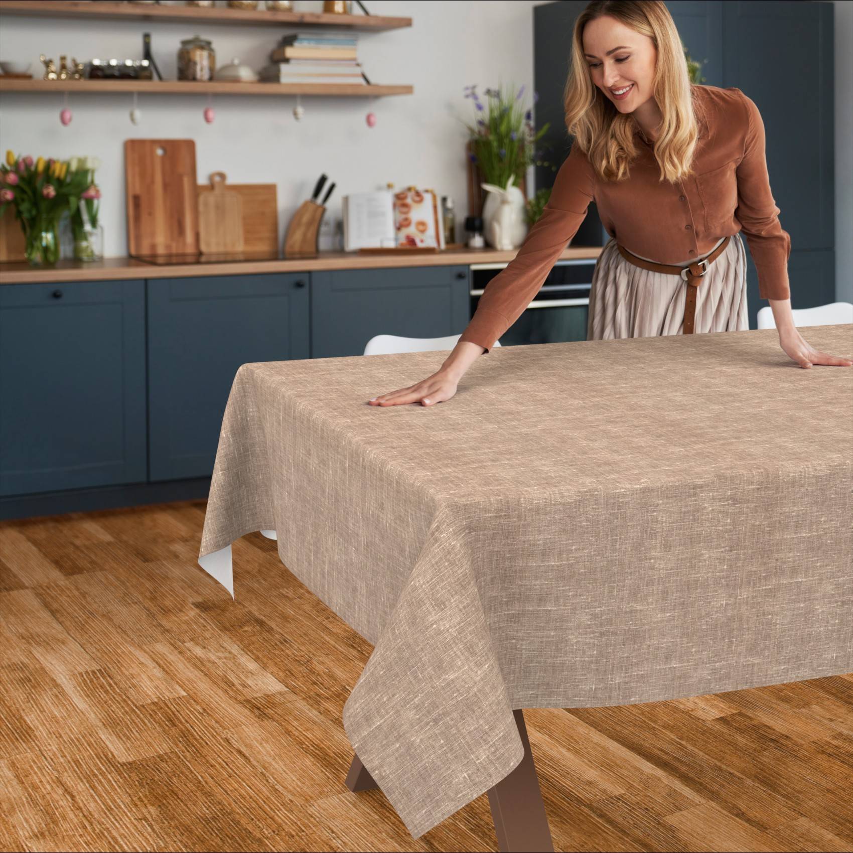 Lächelnde Frau breitet eine beige Tischdecke über einen Esstisch in einer modernen Küche aus.