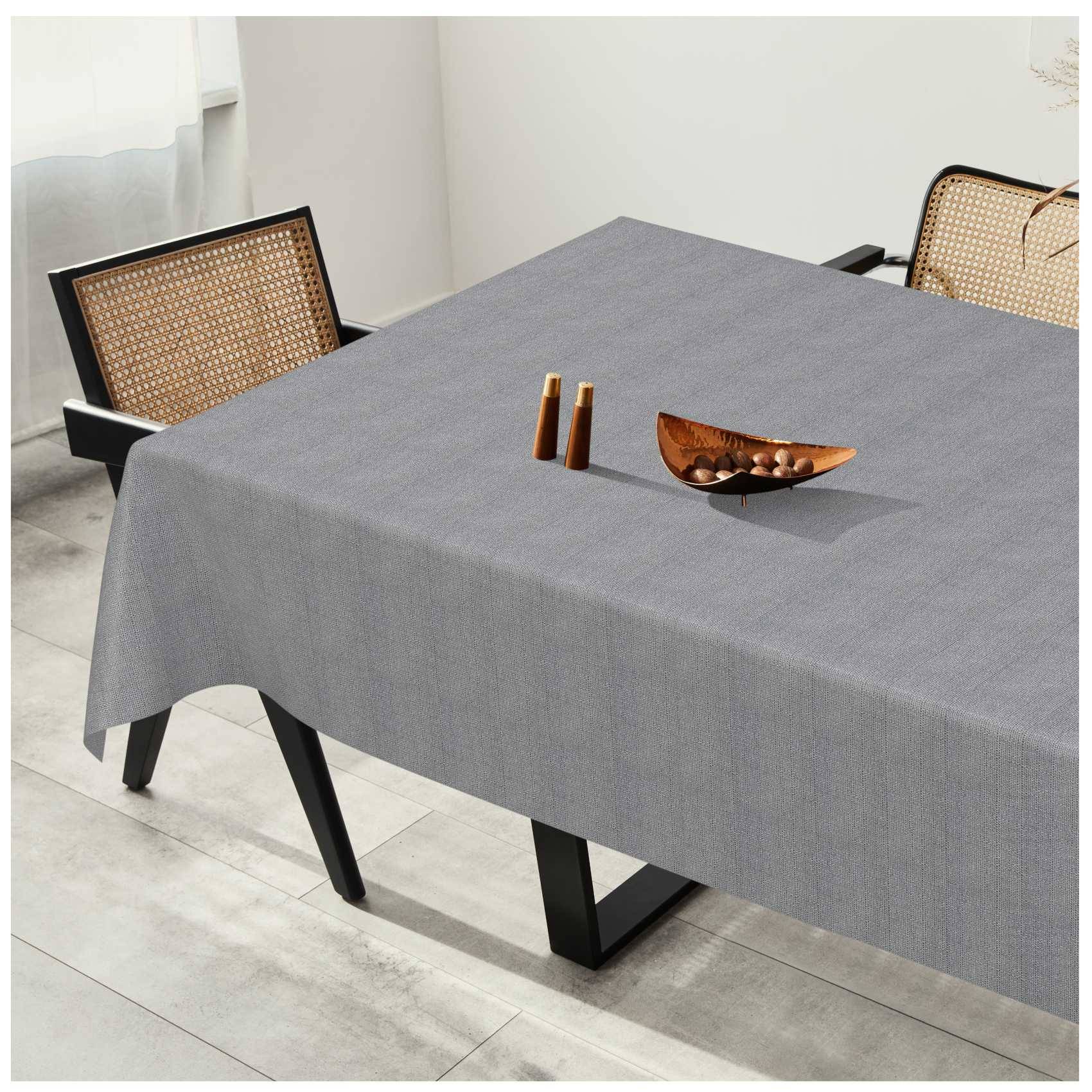 Esstisch mit grauer Tischdecke, ausgestattet mit einer kleinen hölzernen Tischdekoration, umgeben von zwei Stühlen mit Rohrgeflecht-Rückenlehnen in einem hellen Raum.