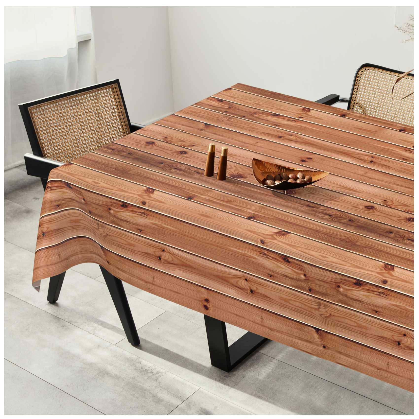 Holzesstisch mit Holzmuster-Tischdecke, schwarzen Stühlen und kleinen Dekorationsgegenständen in einem hellen Raum.