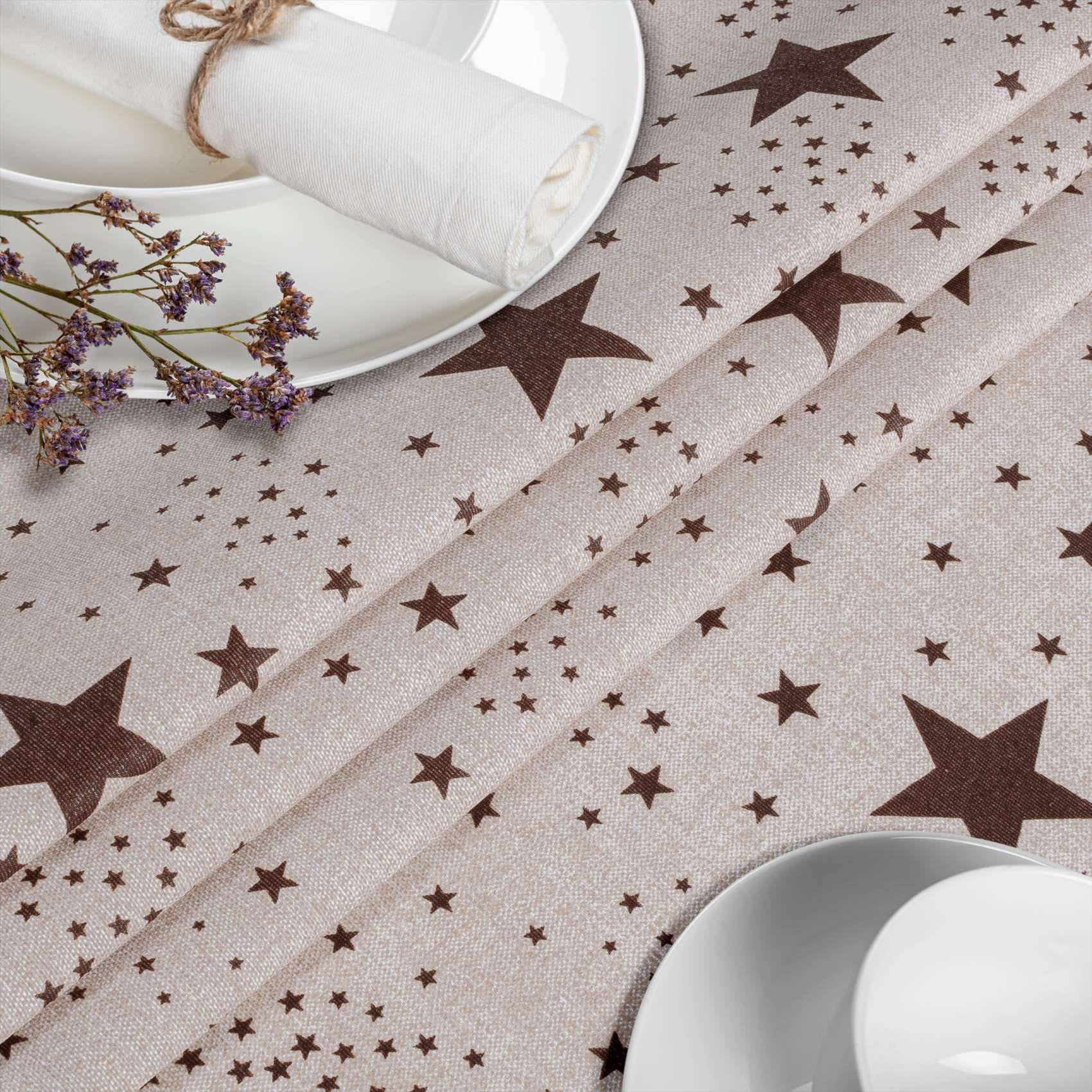 Beige Tischdecke mit Sternmuster, weiße Teller und aufgerollte Servietten, eingedeckt für ein festliches Mahl.