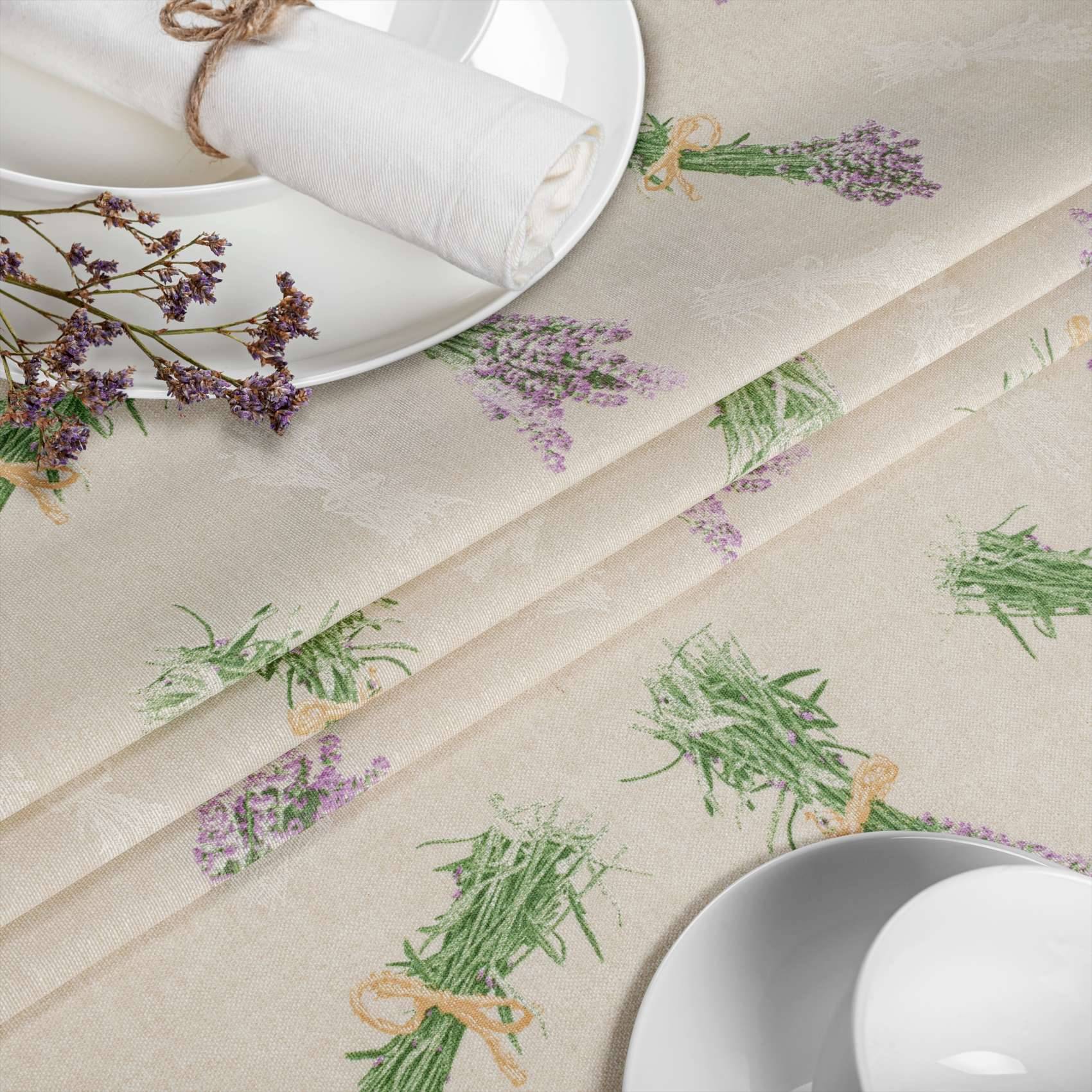 Tischdeckung mit weißen Tellern und gefalteten Servietten auf einer cremefarbenen Tischdecke mit aufgedruckten Lavendel- und grünen Kräuterzweigen.
